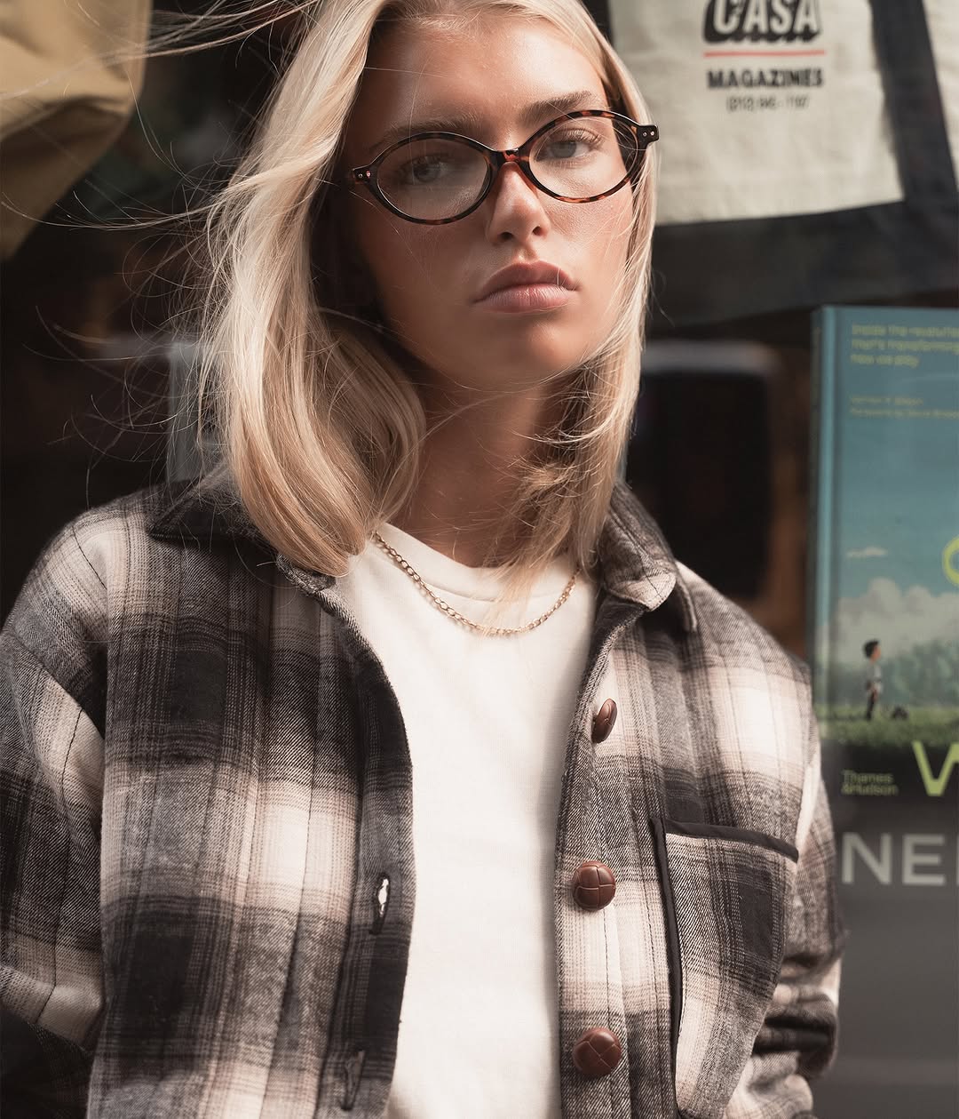 Close-up portrait showing the model wearing the plaid shirt over the white top with glasses.