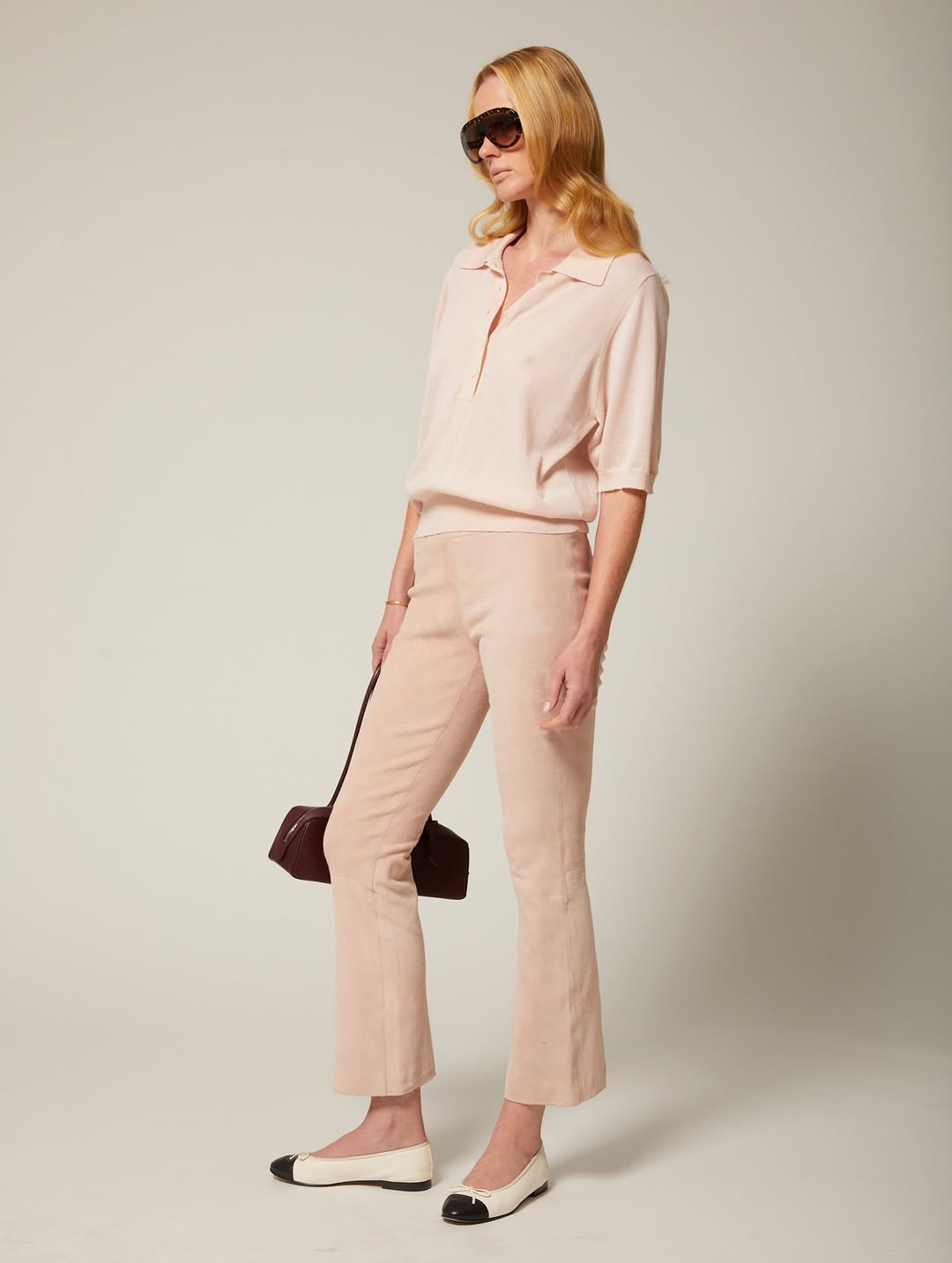 Full-body front/side view of the same pale pink polo shirt and trouser set, styled with two-tone flats and sunglasses.