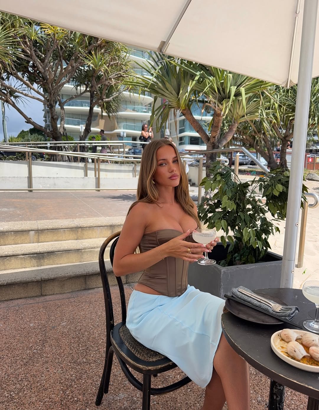 Model seated at a table wearing the same brown corset and blue skirt ensemble.