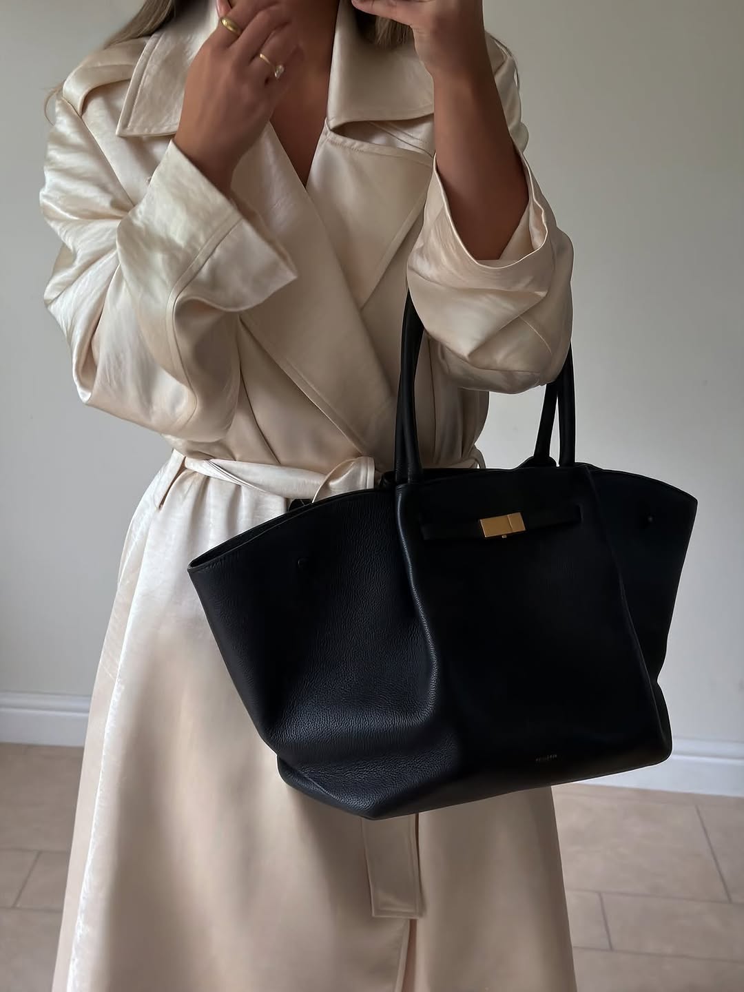 Detail shot focusing on the upper body and hands holding the black tote bag, showing the texture of the cream satin fabric.