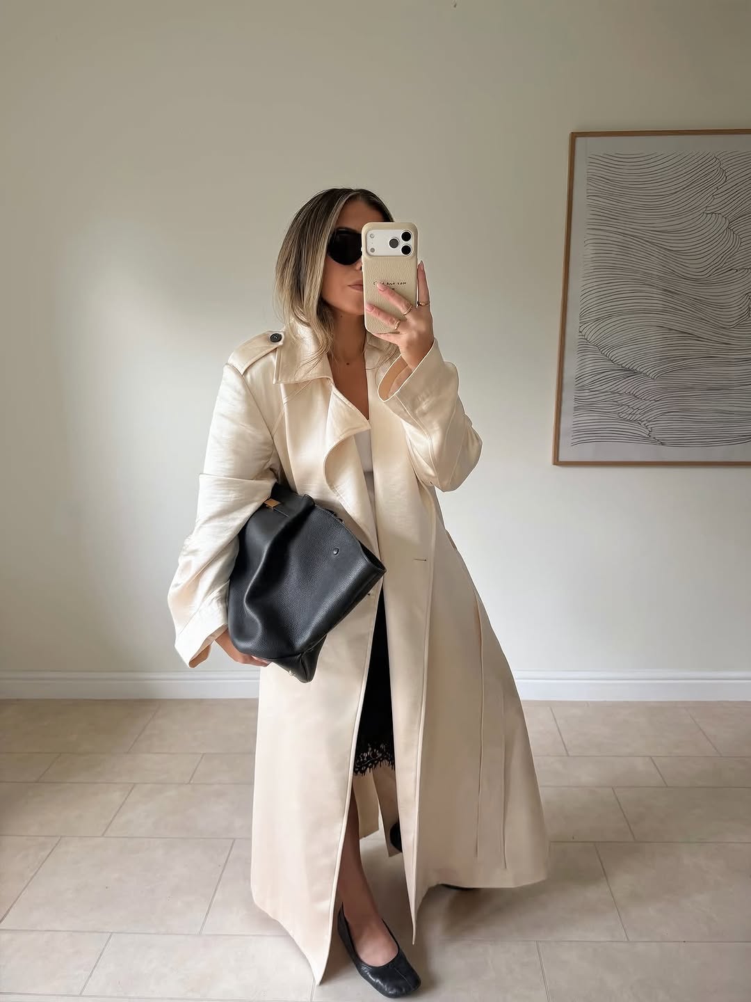 Mirror selfie featuring the same cream trench coat outfit, now accessorized with sunglasses and a large black leather tote bag.