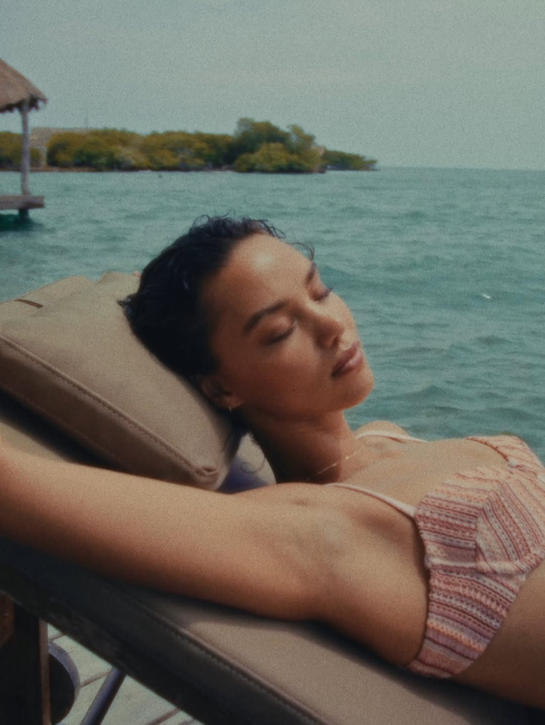 Model reclining on a lounge chair wearing a pink striped bralette top.