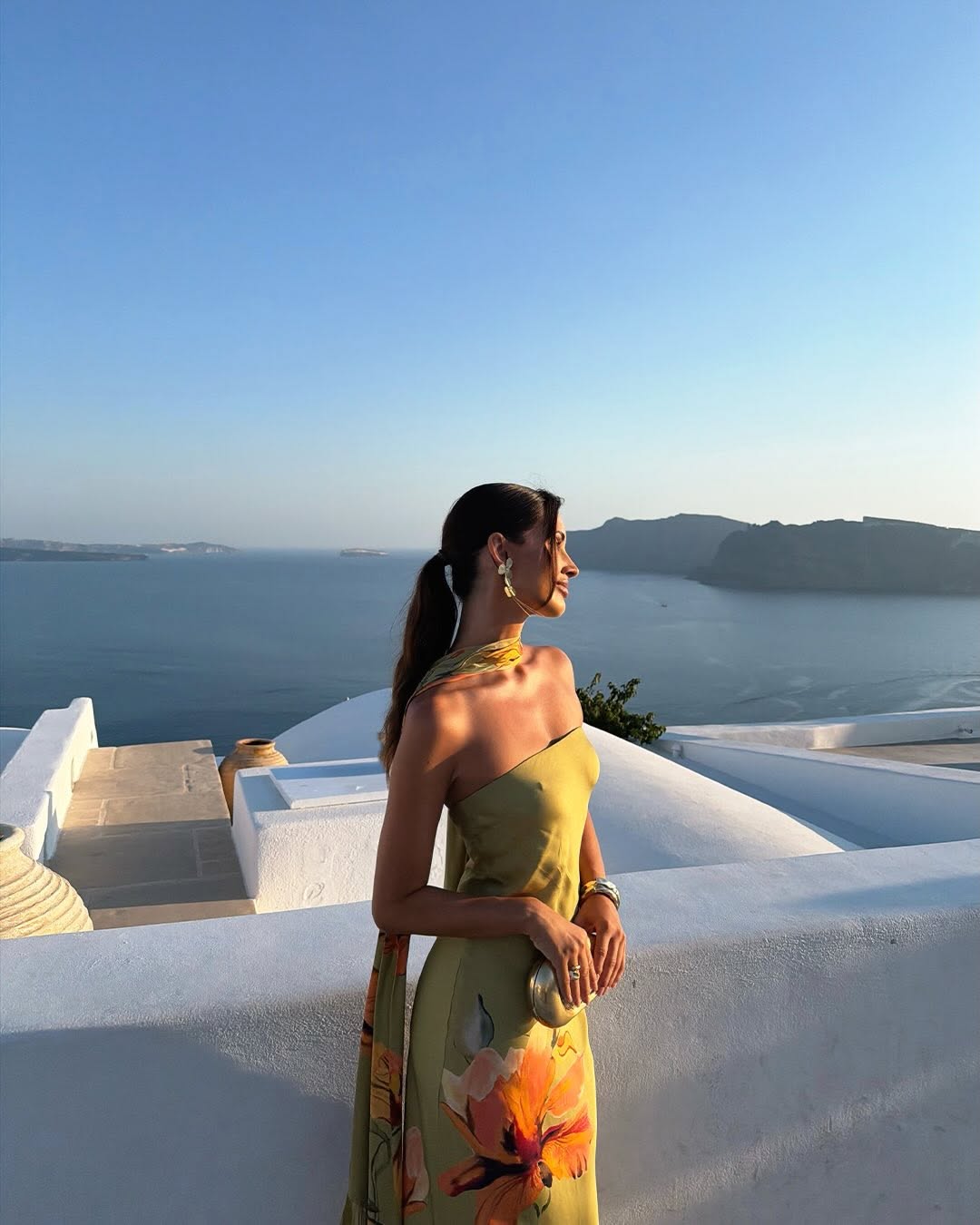 Profile view of the model standing by a white wall, wearing the olive green floral dress.