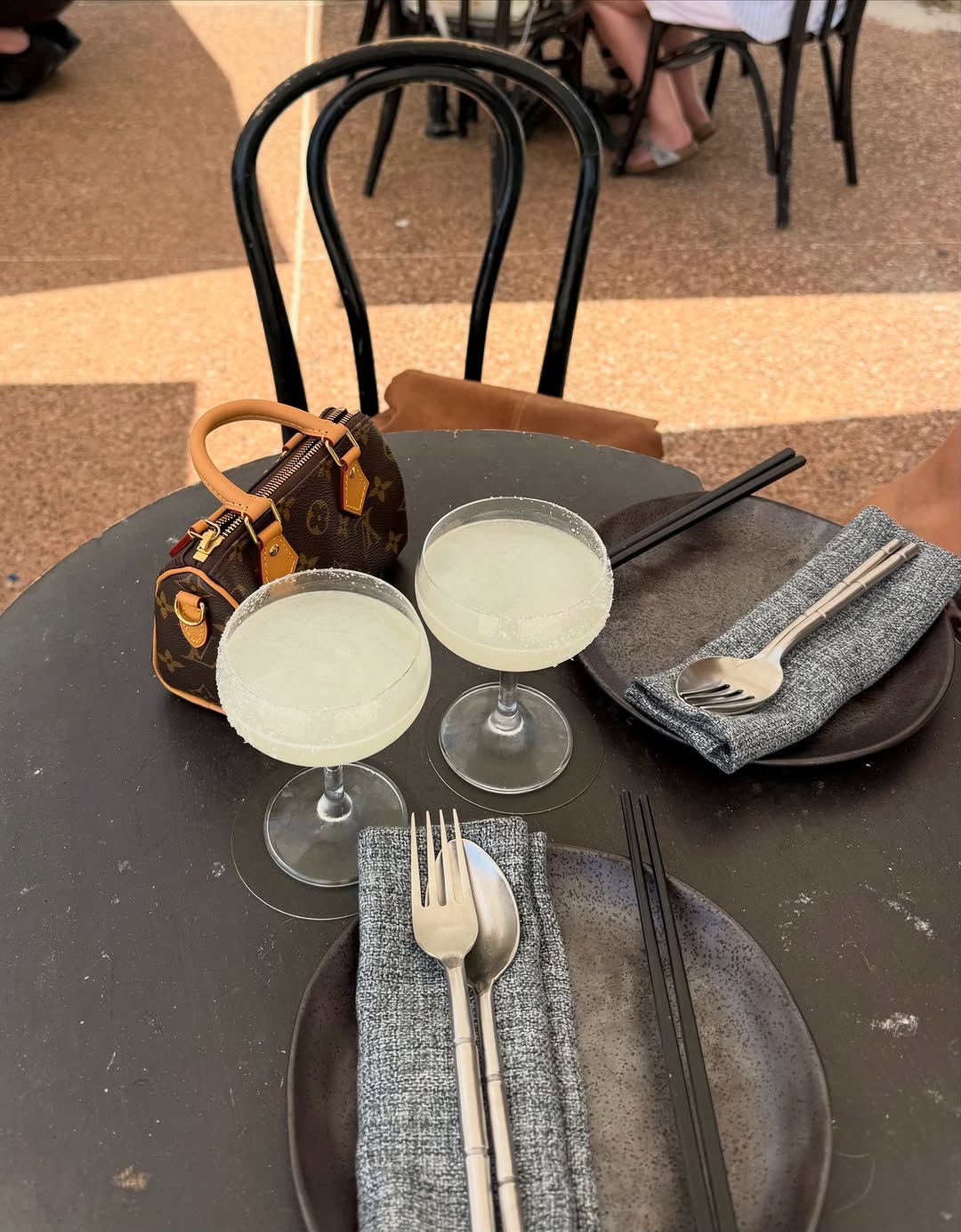 Close-up shot of drinks, cutlery, and a handbag on a table; no clothing visible.