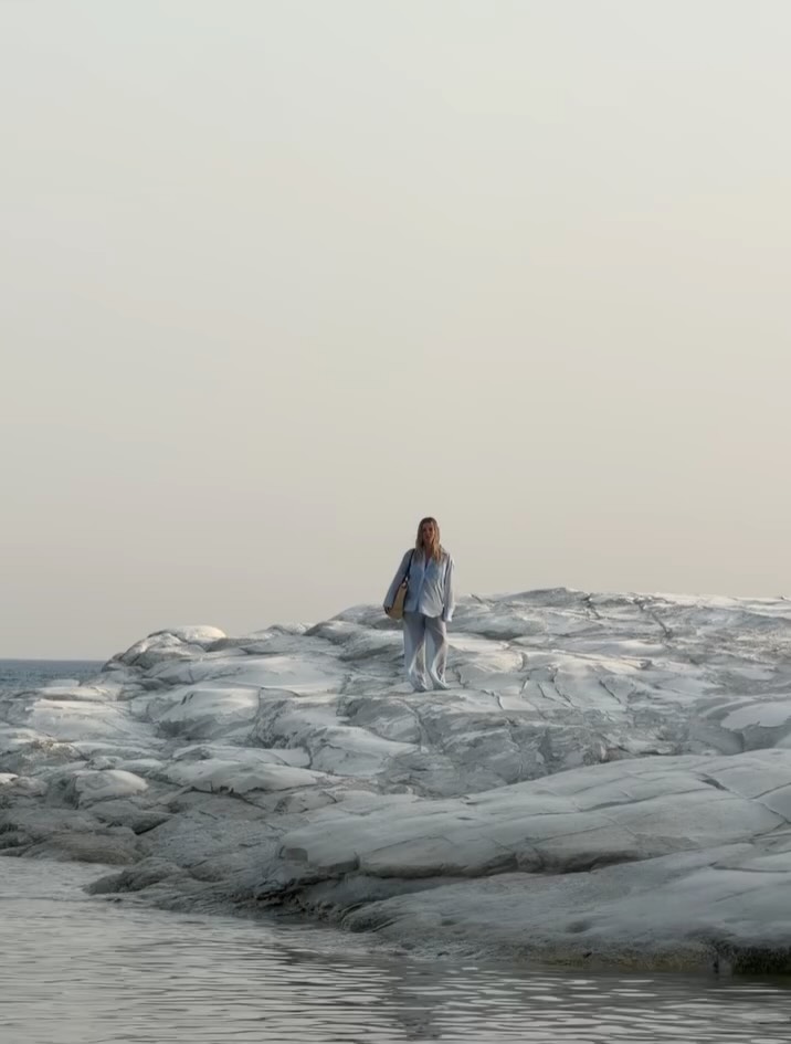 Long-distance front view of the model standing on rocks, wearing the full light blue outfit.