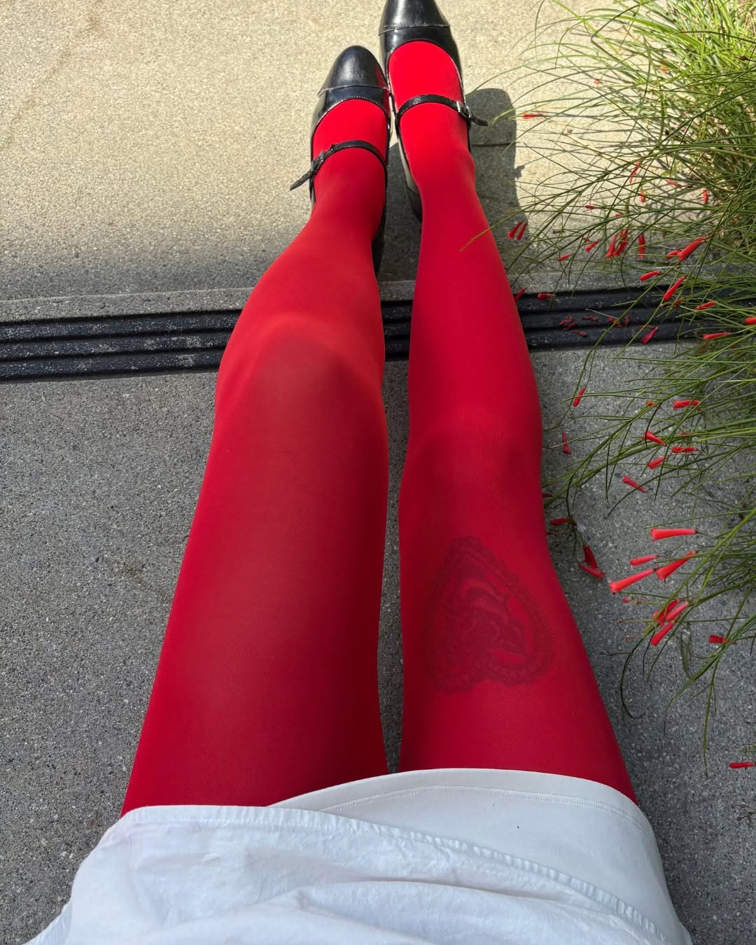 POV close-up looking down at legs extended, highlighting the heart design knit into the red tights and the shoes.
