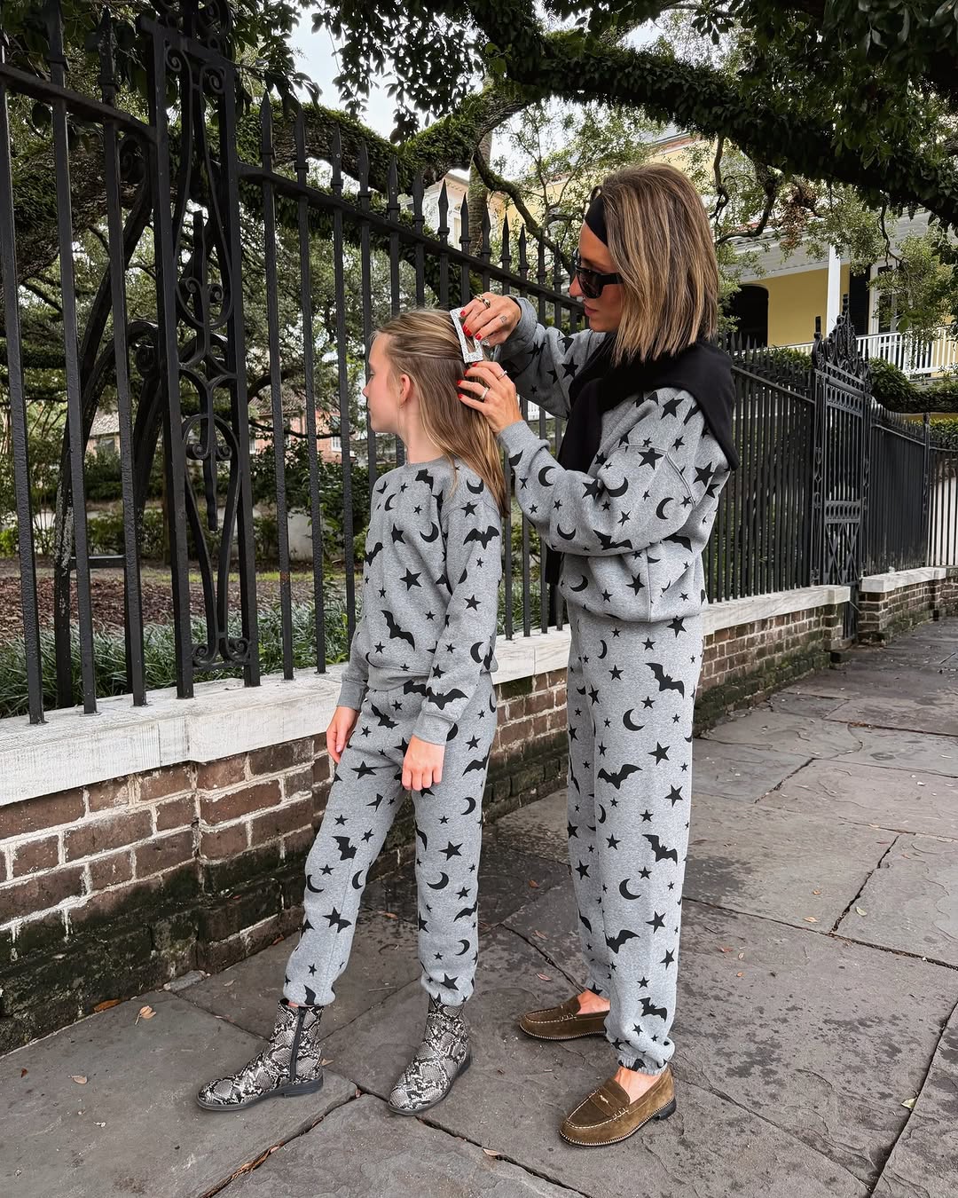 Side profile view of the woman adjusting the girl's hair clip while both wear the celestial-themed matching outfits.