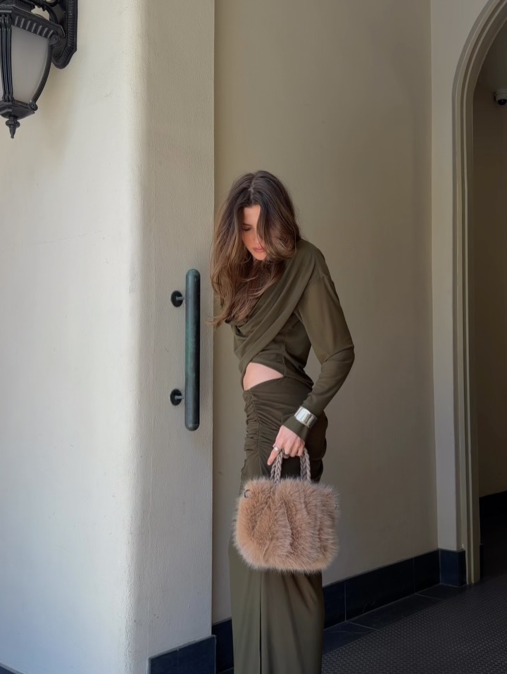 Medium shot showing the full silhouette of the olive green two-piece set with fur bag styling.