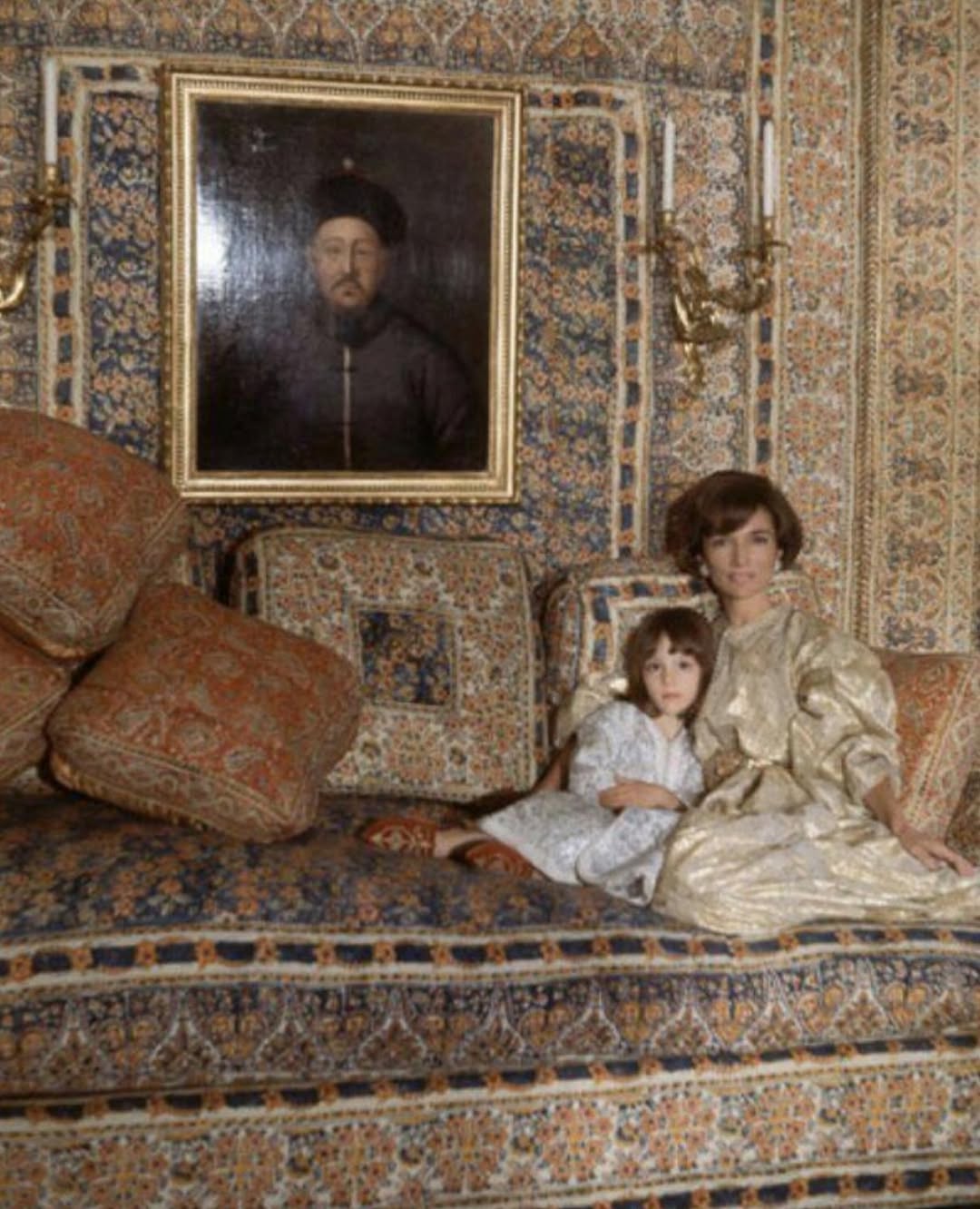 Mood image of Jackie Kennedy sitting on a couch covered in ornate fabric.