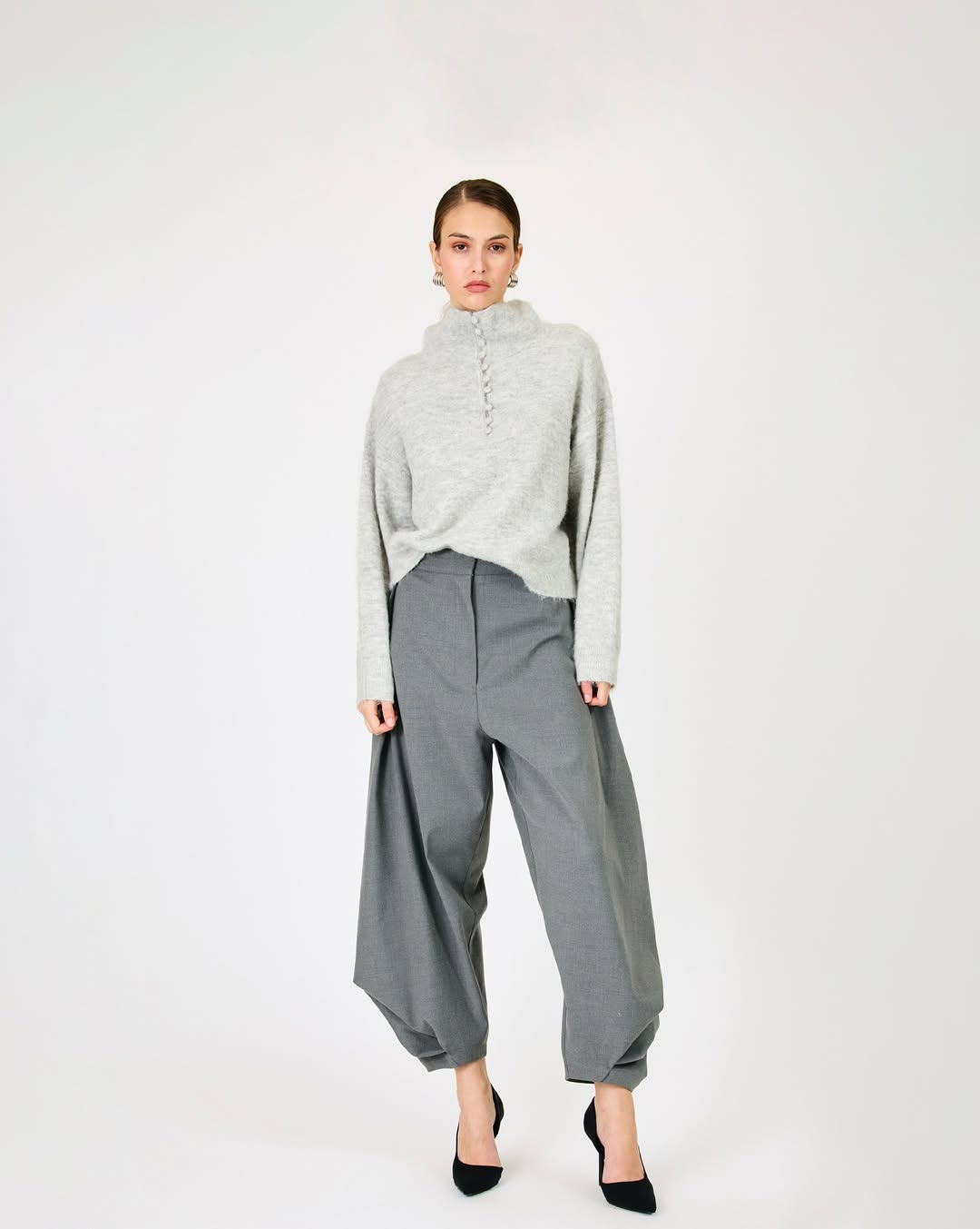 Full-body shot of the model in the same light grey buttoned sweater, grey balloon-leg trousers, and black heels.
