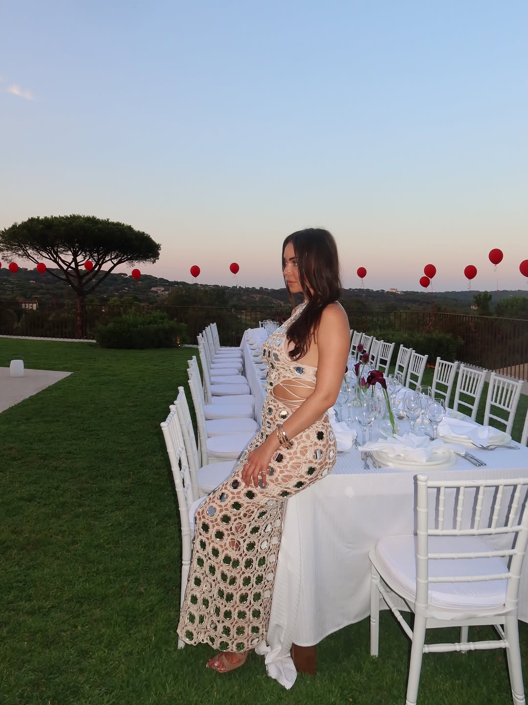 The model leaning against an outdoor dining table, displaying the full length and fit of the dress.