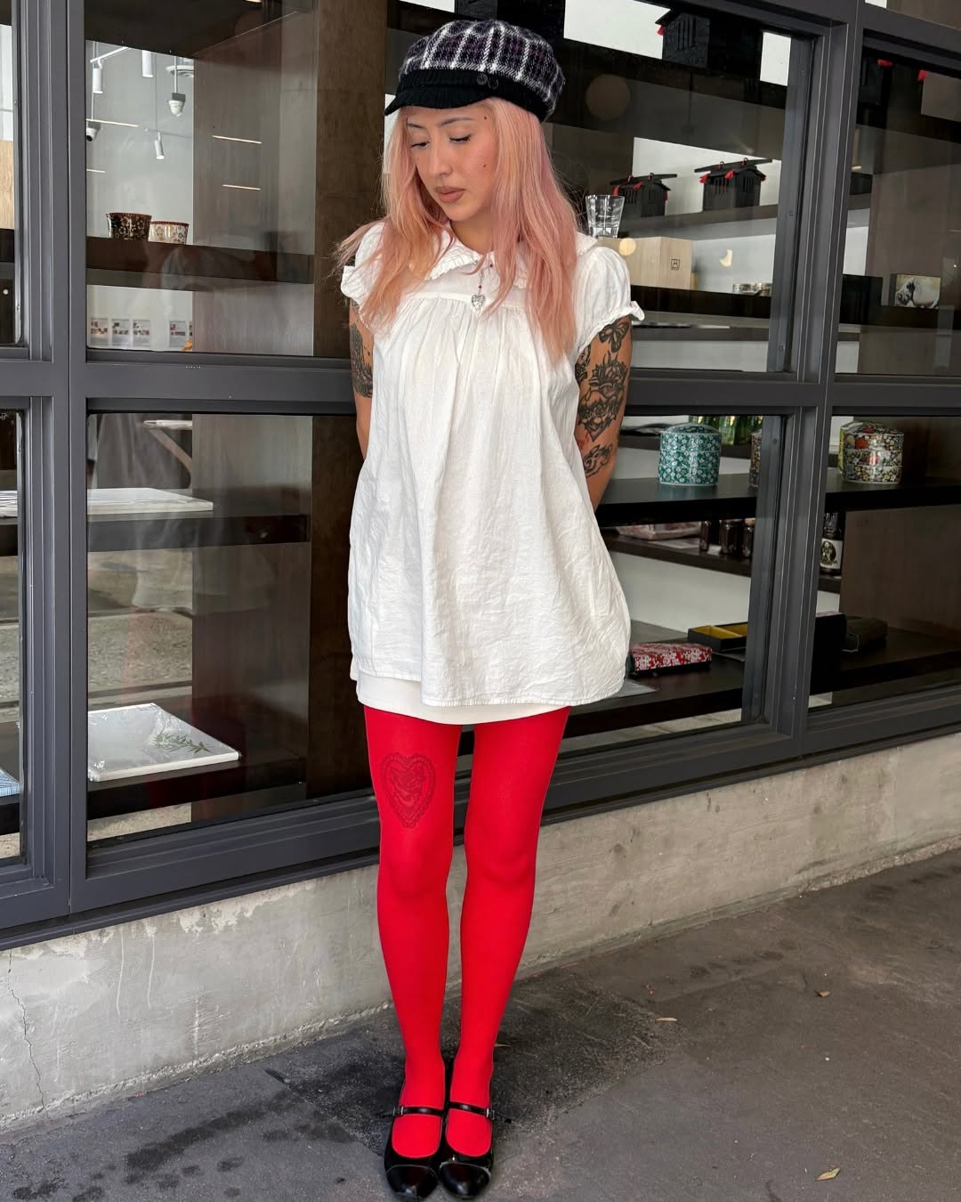 Full-body shot of the model standing in front of a window display, adding a plaid newsboy cap to the outfit.