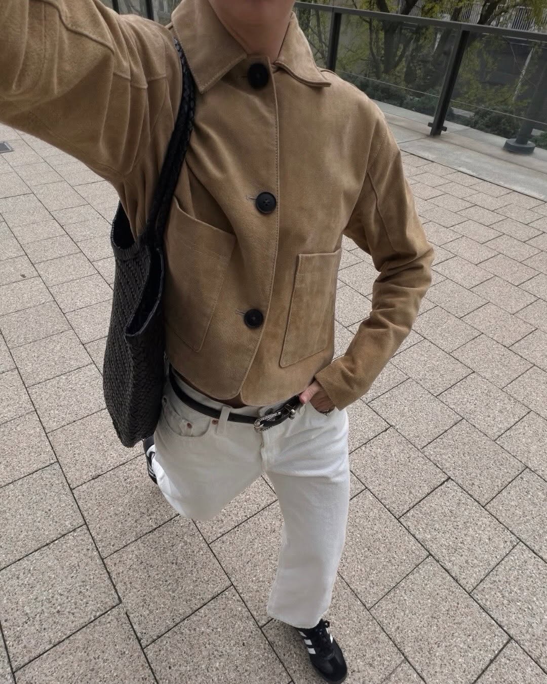 Close-up selfie angle showing details of the tan suede jacket's collar, button closure, and patch pockets, paired with the same white trousers and black belt.