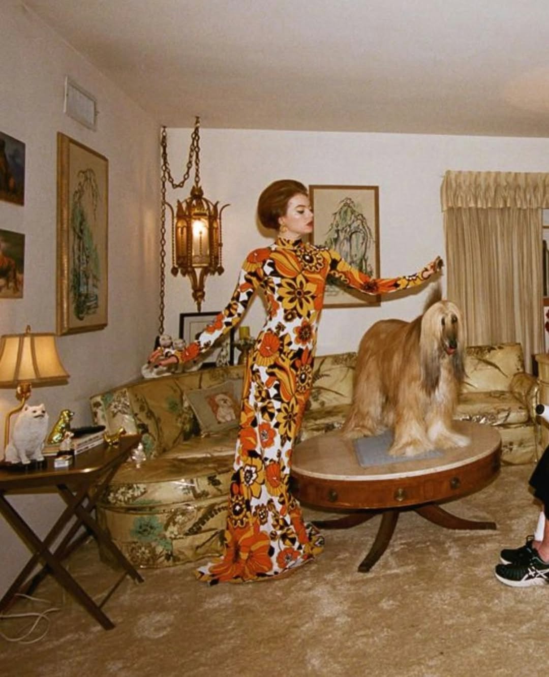 Mood image showing a woman in an orange patterned jumpsuit posing with a dog in a vintage room.