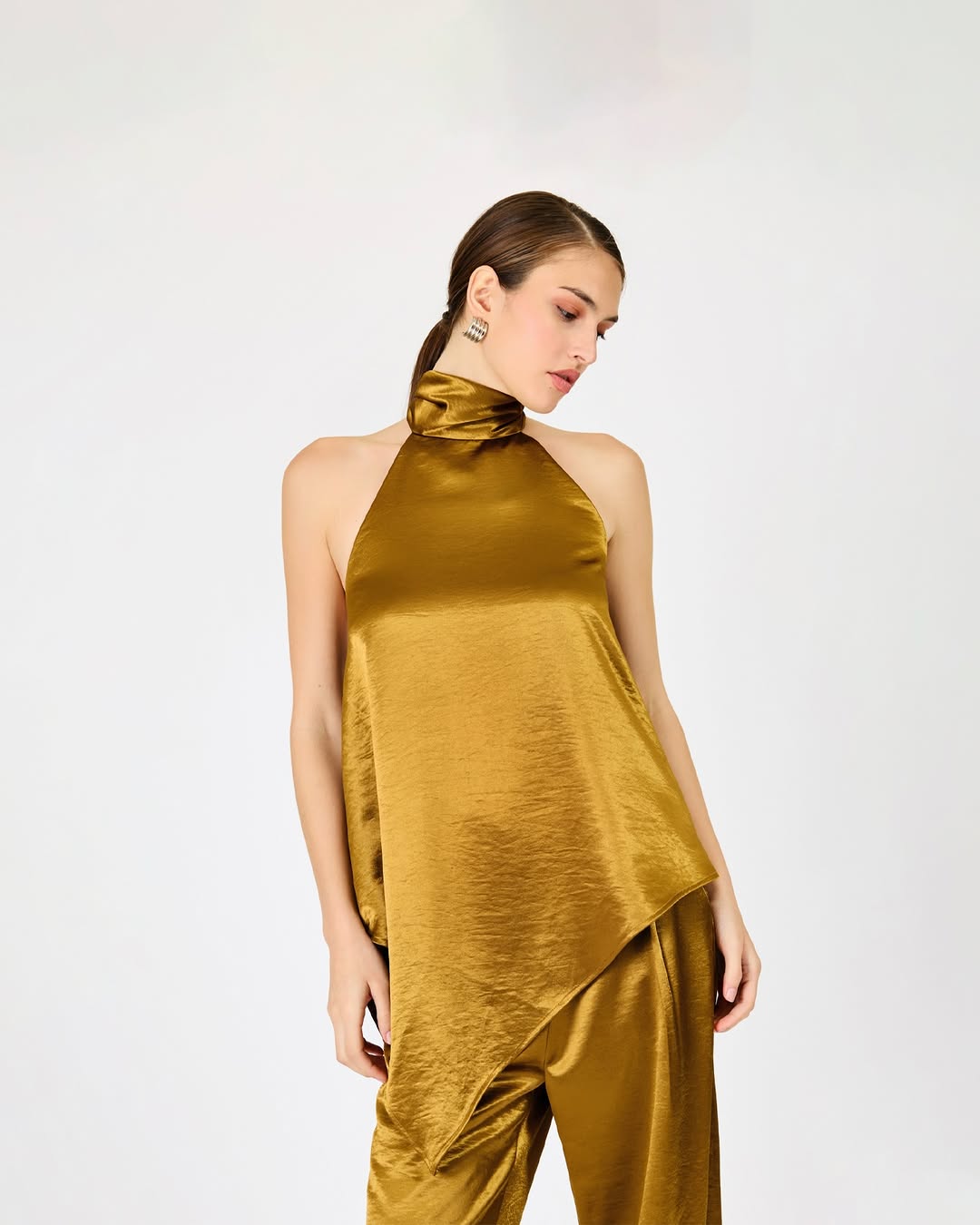 Close-up side view of the same gold satin-like halter top, highlighting the draped neckline and fabric texture.