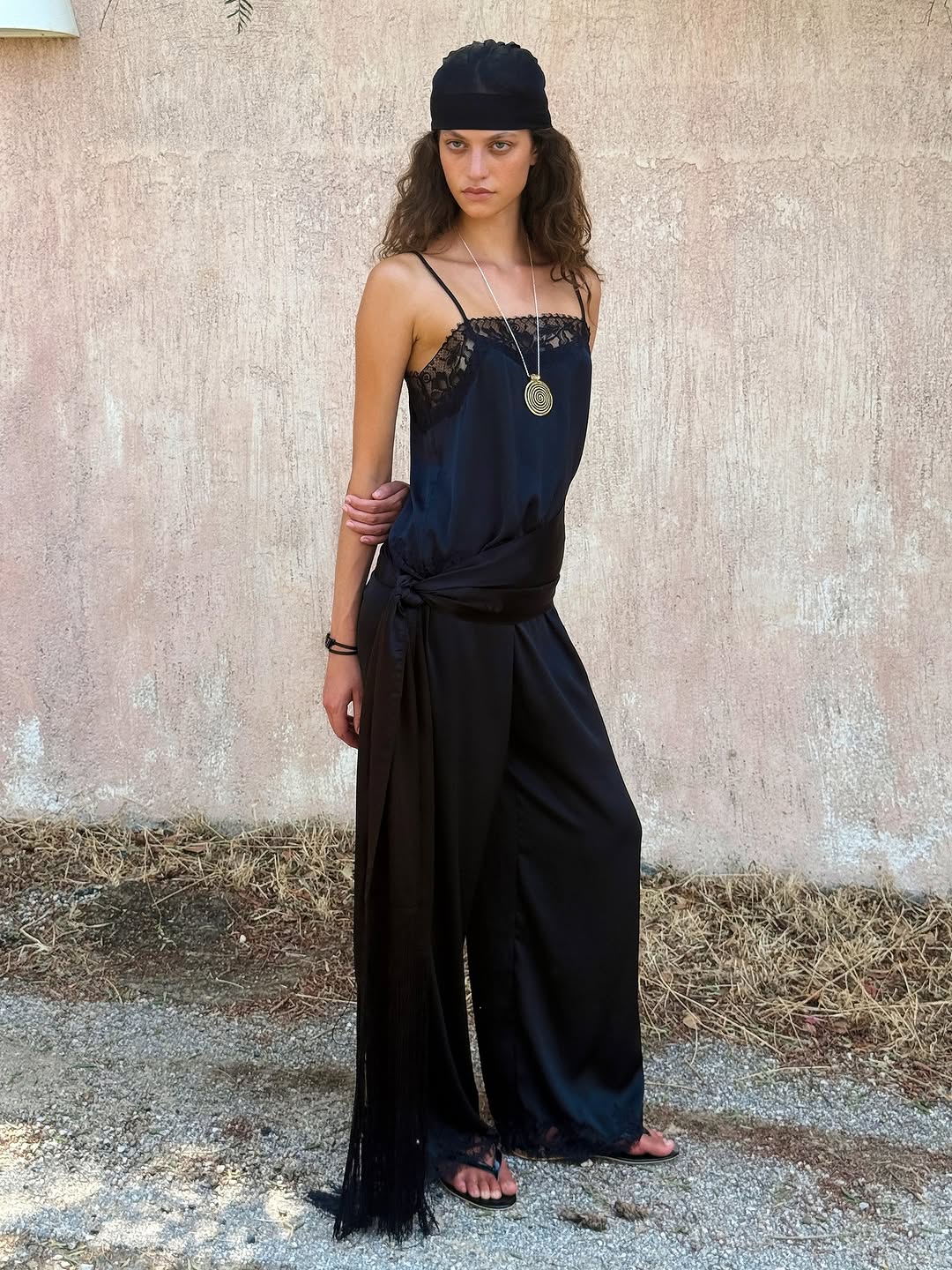 Full-body shot of the model wearing the black camisole tucked into wide-leg trousers with a long sash belt.