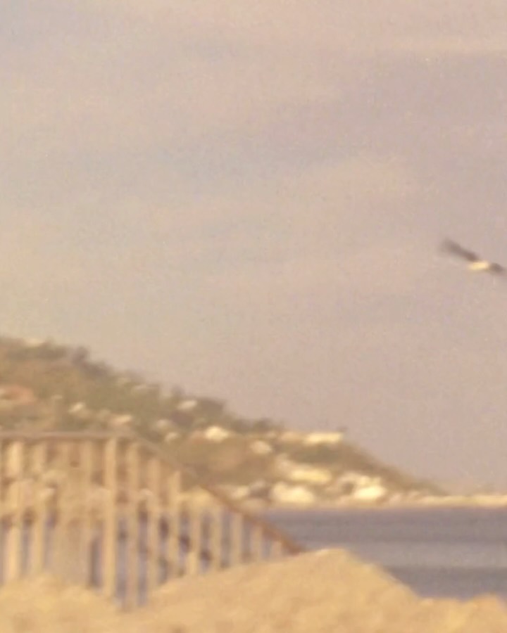 Blurry landscape photo of a coastline and sky; no fashion subject visible.