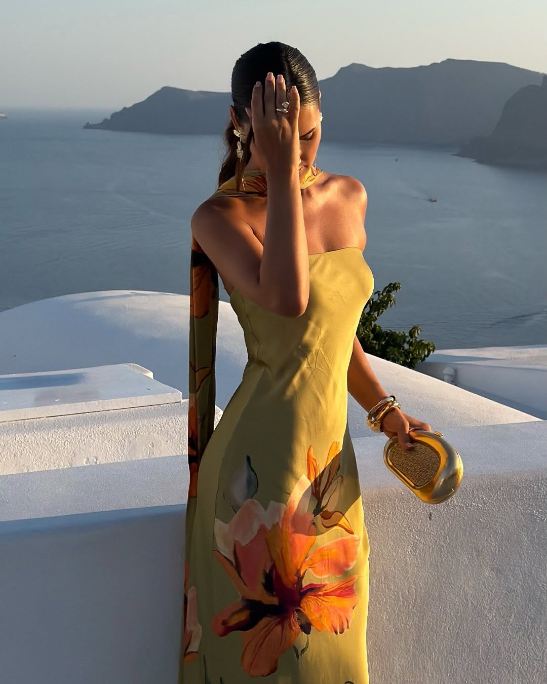 Side view of the model in the same olive green floral dress holding a gold clutch.