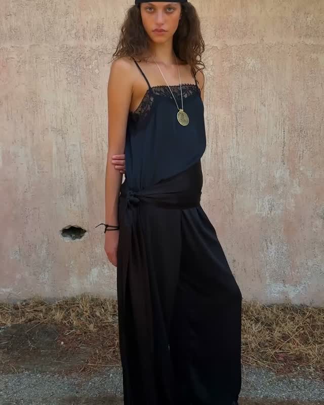 Three-quarter view of the model in the same black camisole and trouser set, accessorized with a gold necklace.