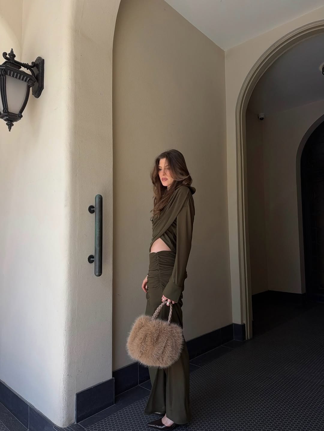 Full-body profile view of the model wearing the olive green draped shirt and skirt ensemble.