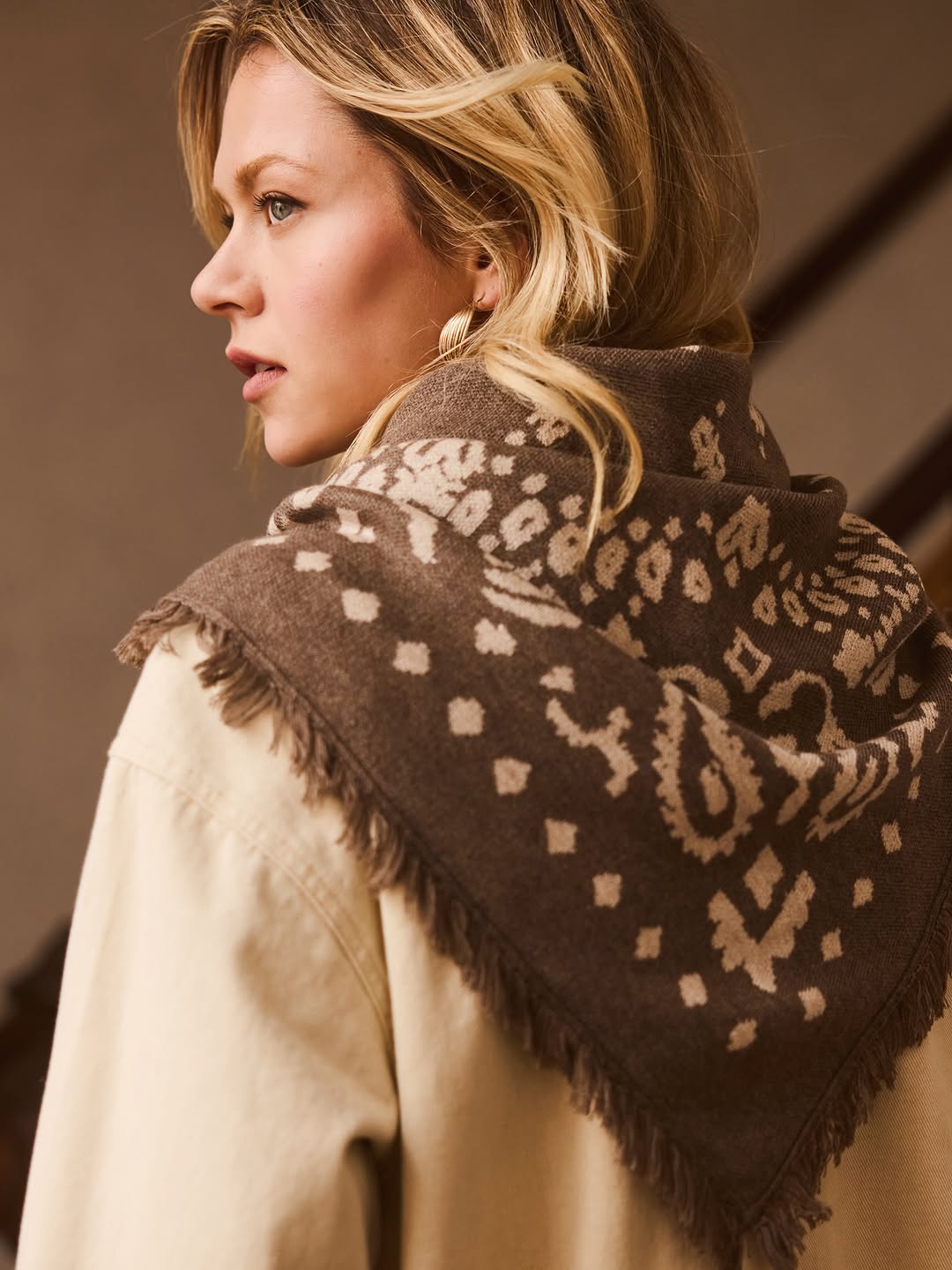 Close-up side profile of the model showing the texture and fringe details of the brown patterned scarf.