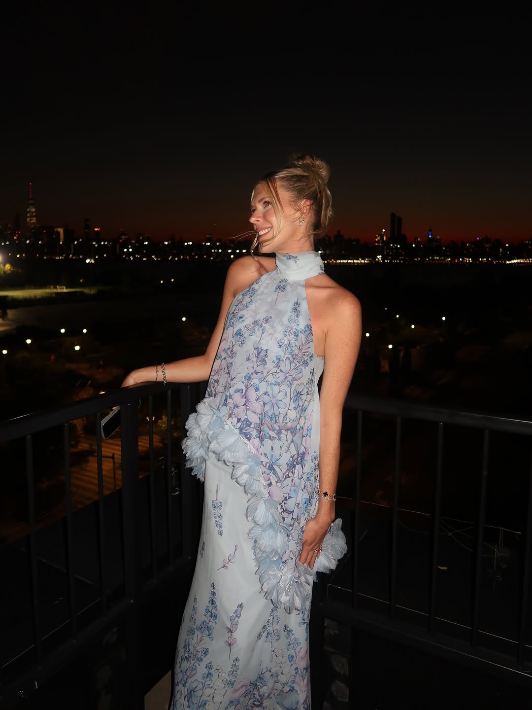 Nighttime shot of the dress against a city skyline, focusing on the halter neck and sheer floral bodice.