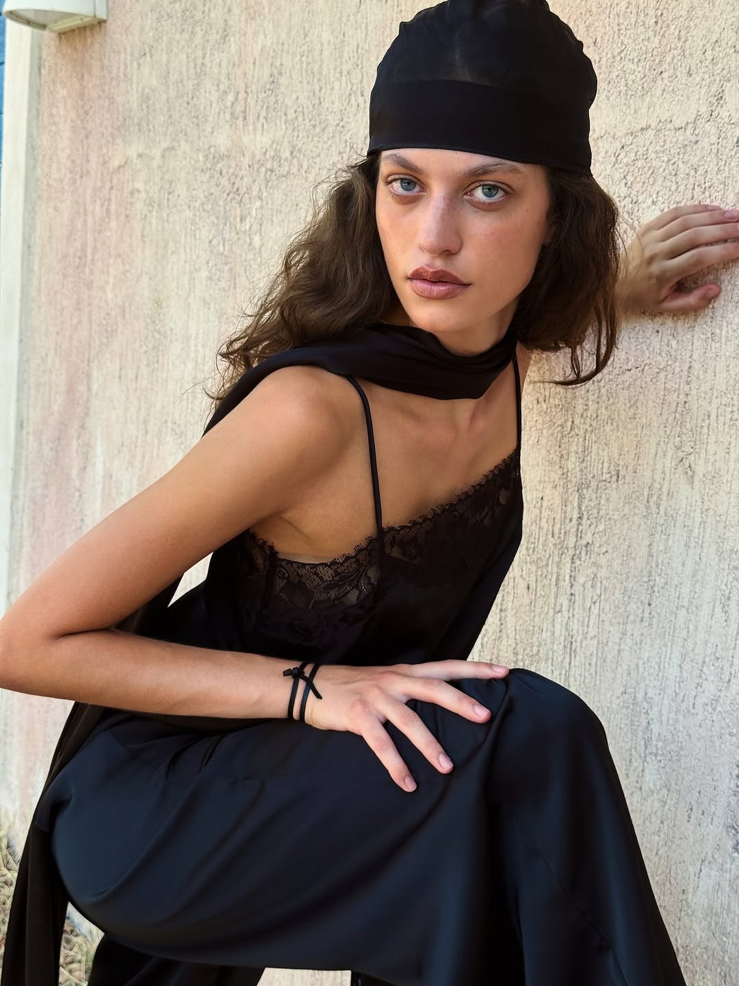 Crouching pose showing the back detail of the black camisole and the drape of the trousers.