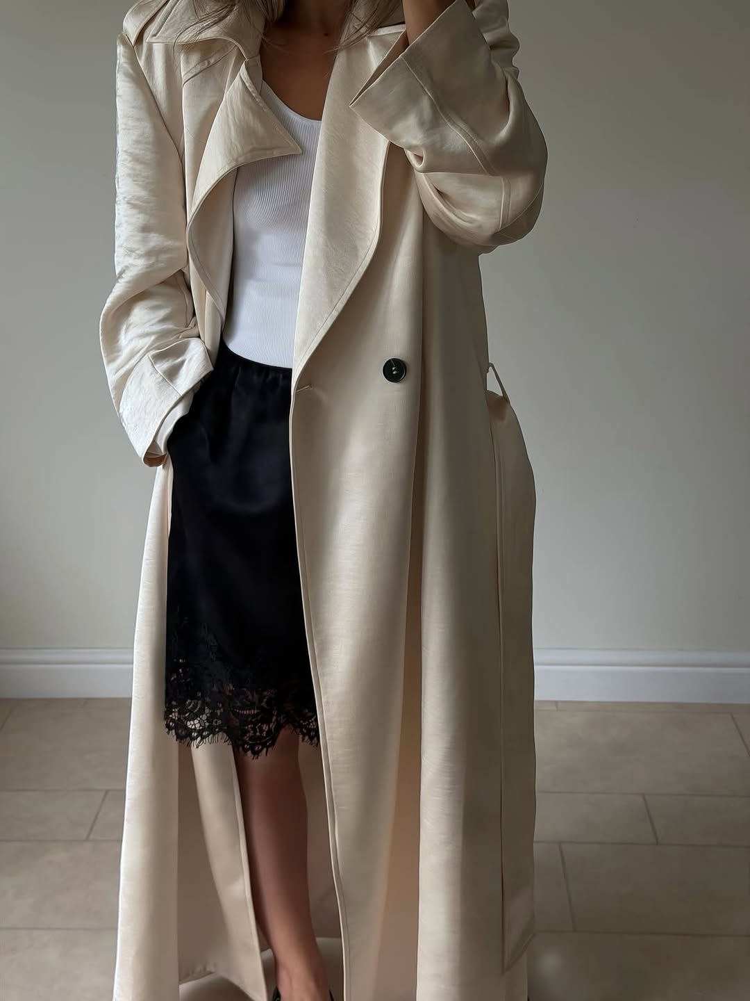 Close-up detail shot of the open front of the cream trench coat, highlighting the lapel, button, and inner layers.
