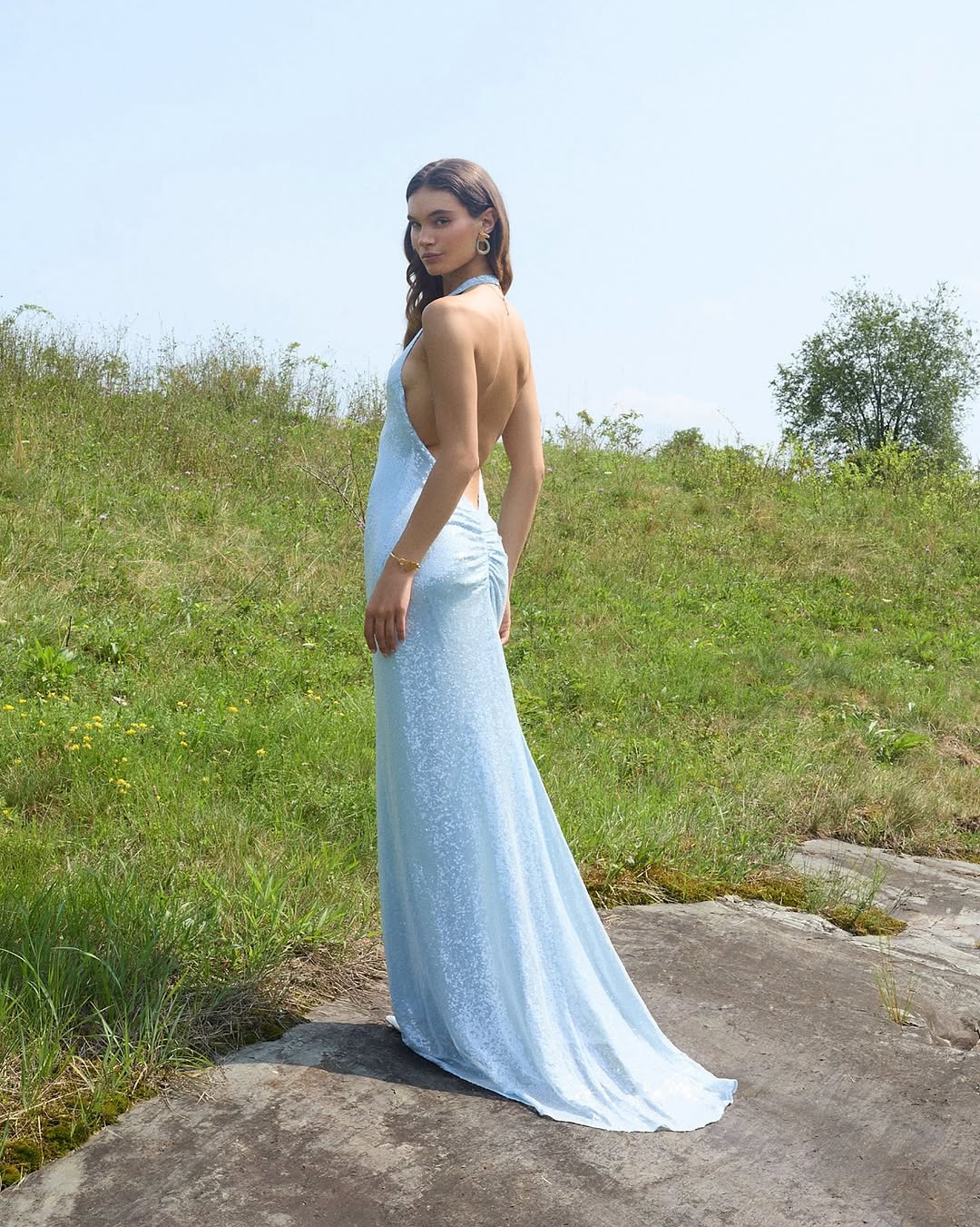 Side profile view outdoors showing the silhouette and ruched detailing of the blue sequined dress.