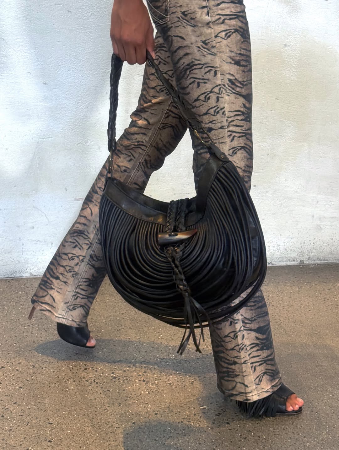 Low-angle shot of legs walking while carrying the bag by its handle, highlighting the fringe movement.