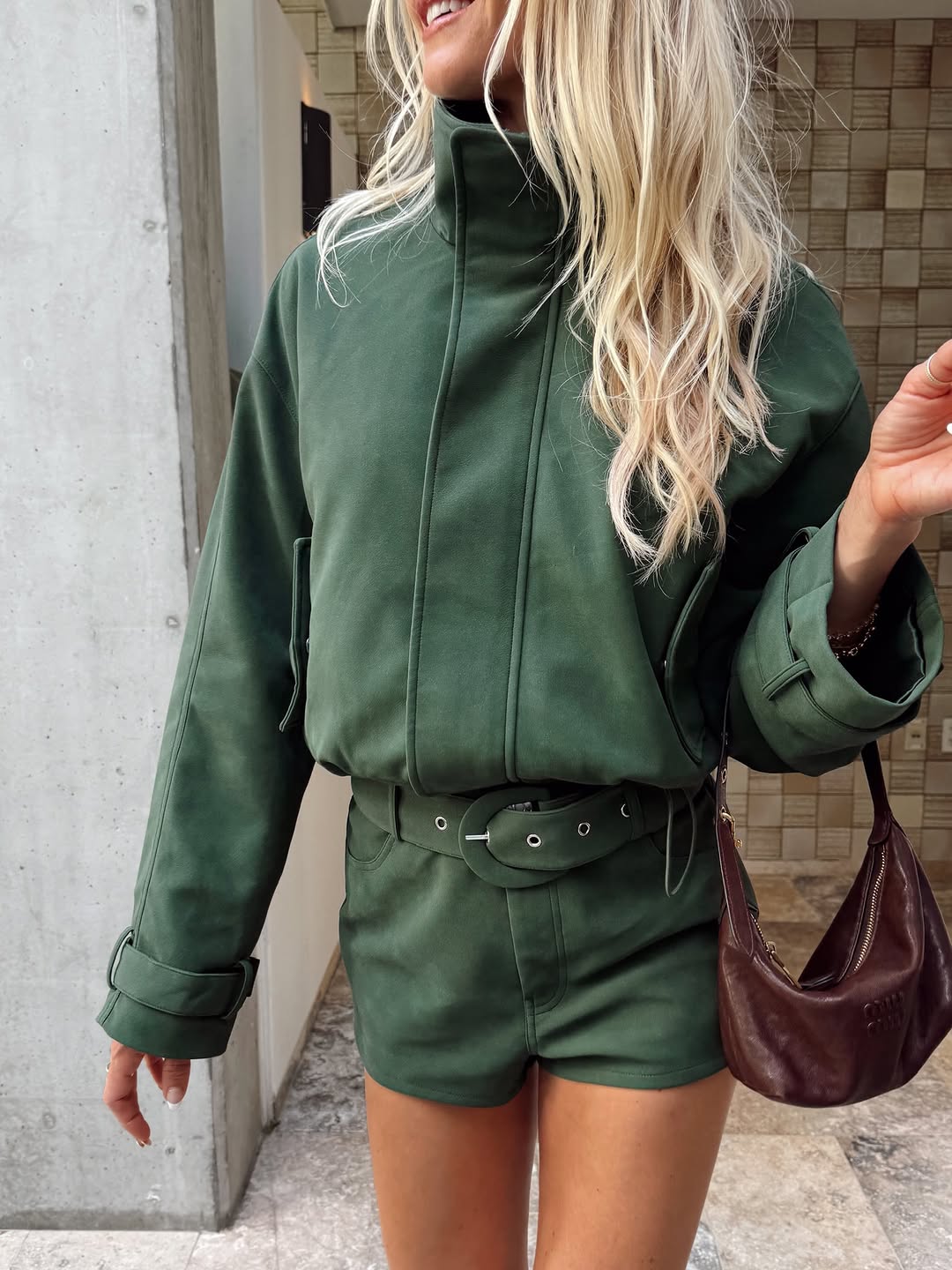 Close-up of torso showing the green suede jacket with high collar and belt detail on shorts.