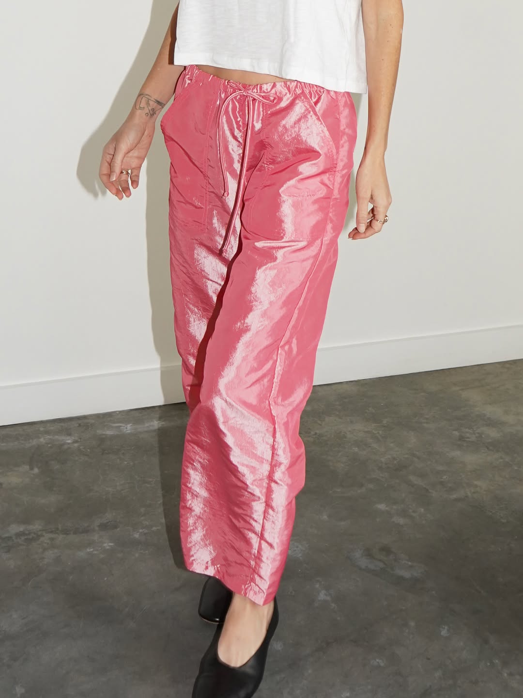 Pink metallic-finish satin pants worn with a white top.