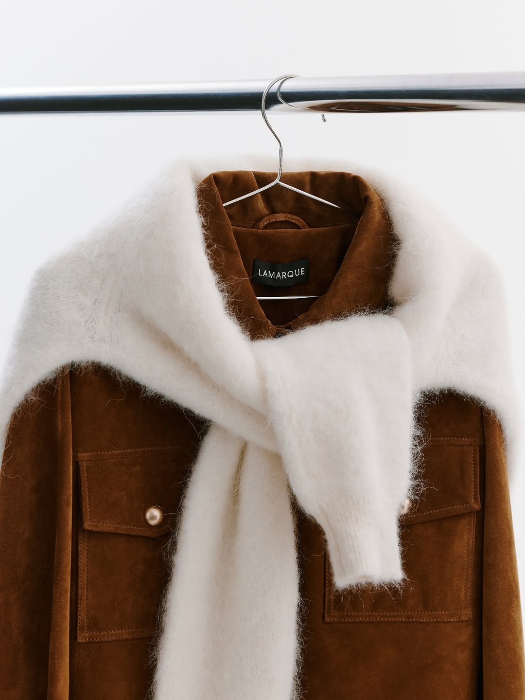 A close-up shot of the upper portion of the same brown suede jacket, highlighting the texture and the styling of the cream sweater draped over the shoulders.