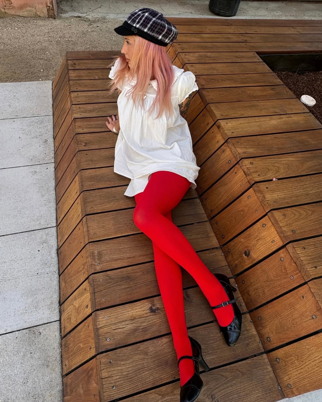 High-angle shot of the model sitting on wooden steps, showing the full silhouette including the hat and loose white tunic.