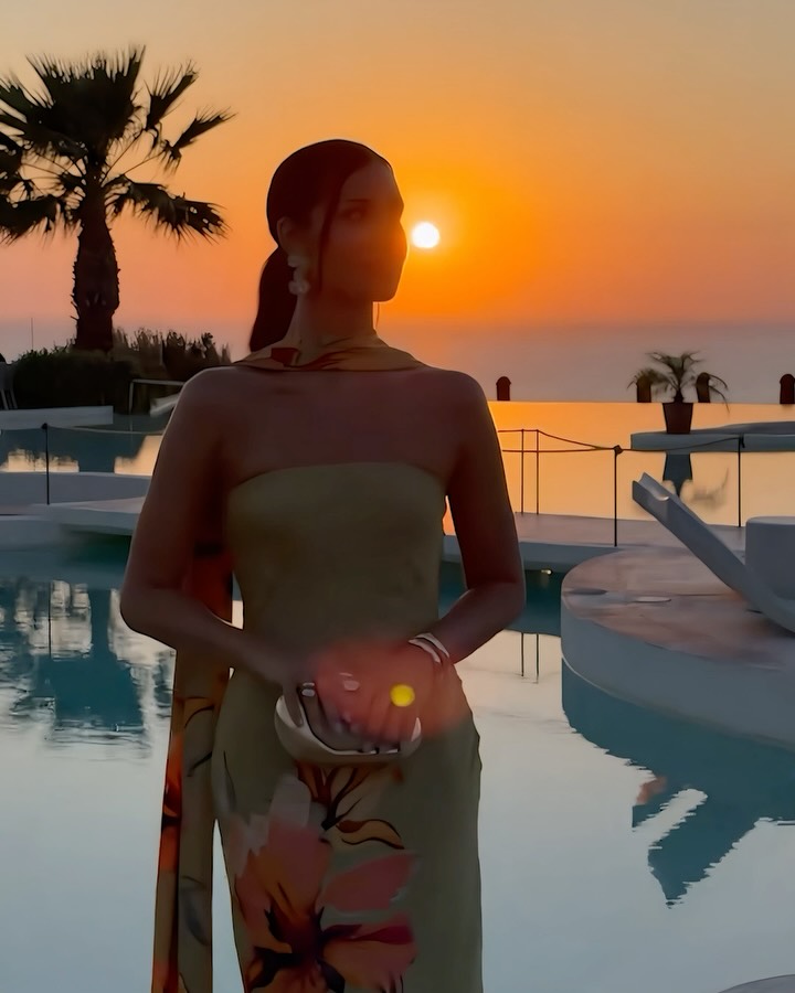 Silhouette of the model in the olive green floral dress against a sunset background.
