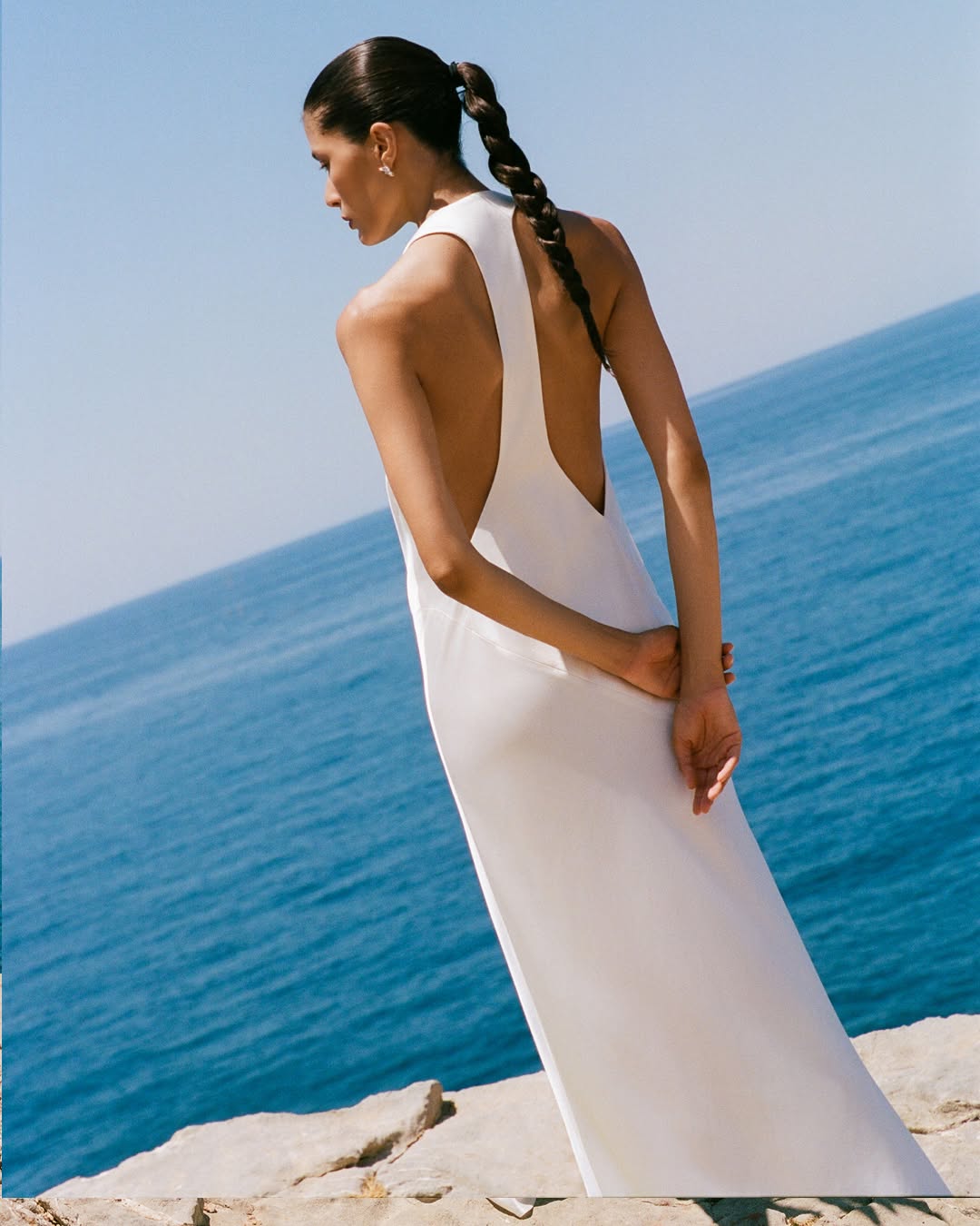 Rear view highlighting the deep V-shaped open back of the white satin dress.
