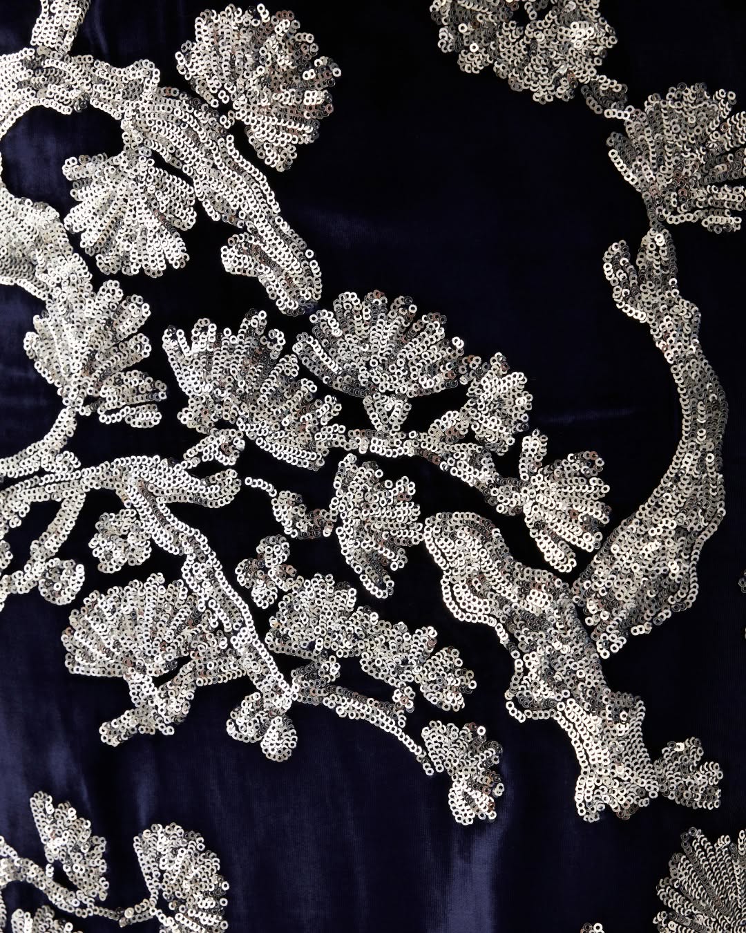 Close-up view of the dark blue velvet fabric with intricate silver sequin floral or pine branch patterns.
