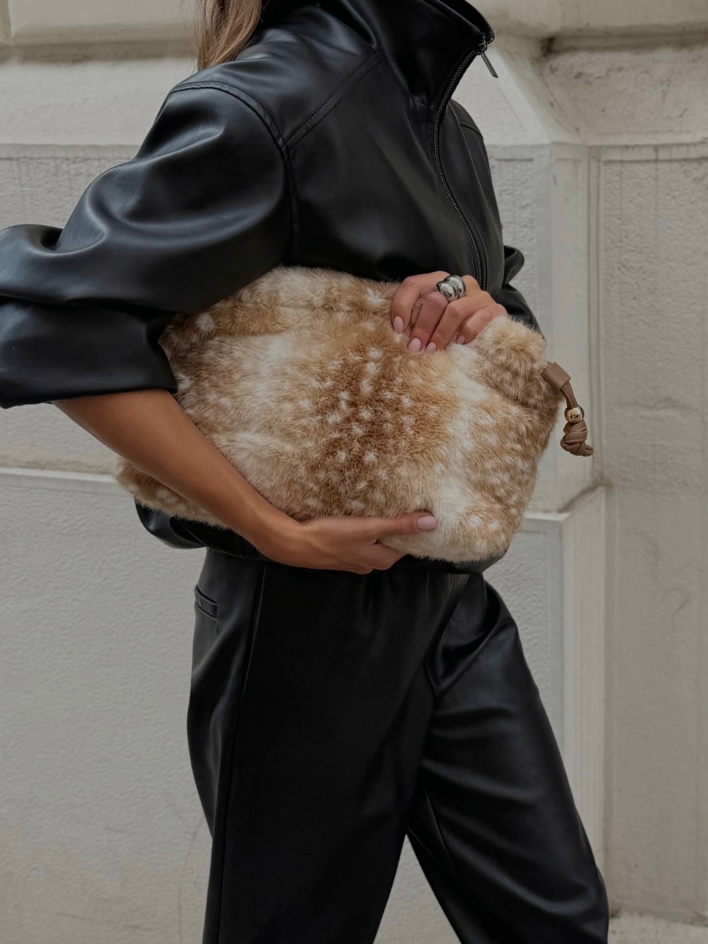 Side profile close-up showing the fit of the leather jacket sleeve and the texture of the spotted fur bag held against the hip.