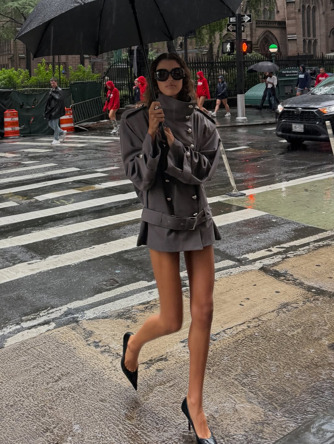 Model crossing a street holding an umbrella, wearing the grey jacket and skirt.