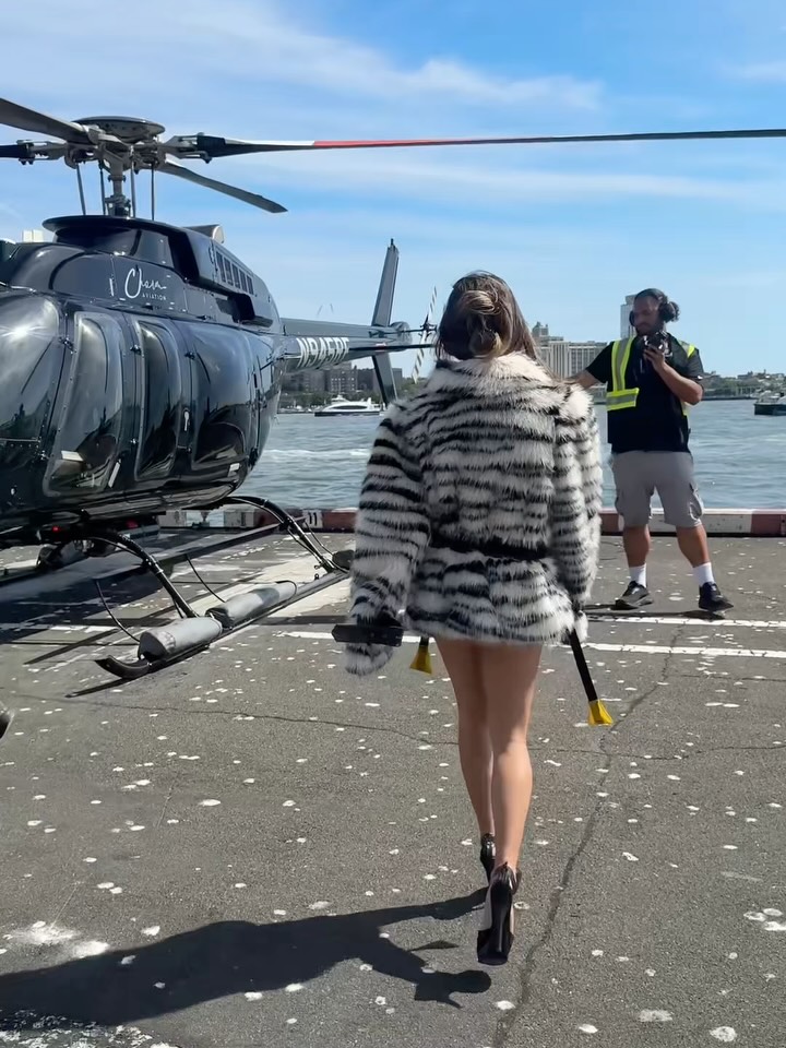 Rear view of the model walking towards a helicopter, displaying the back pattern of the striped faux fur coat.