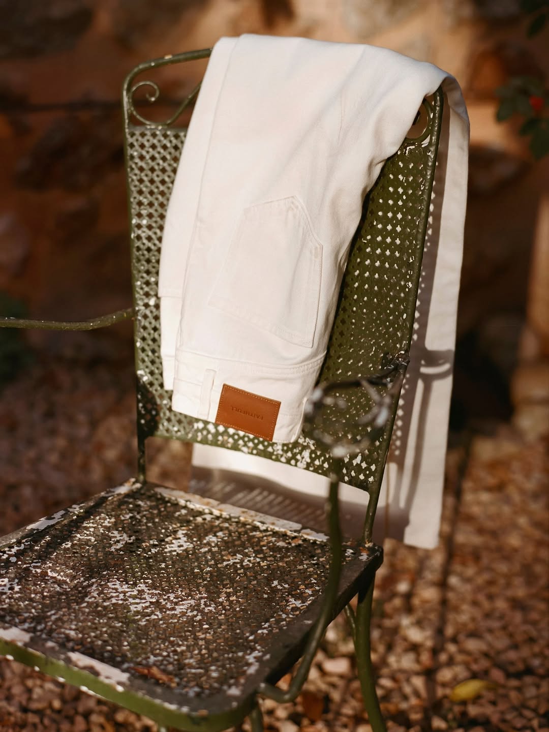 Detail shot of the white denim jeans draped over a chair, showing the back pocket and waistband label.