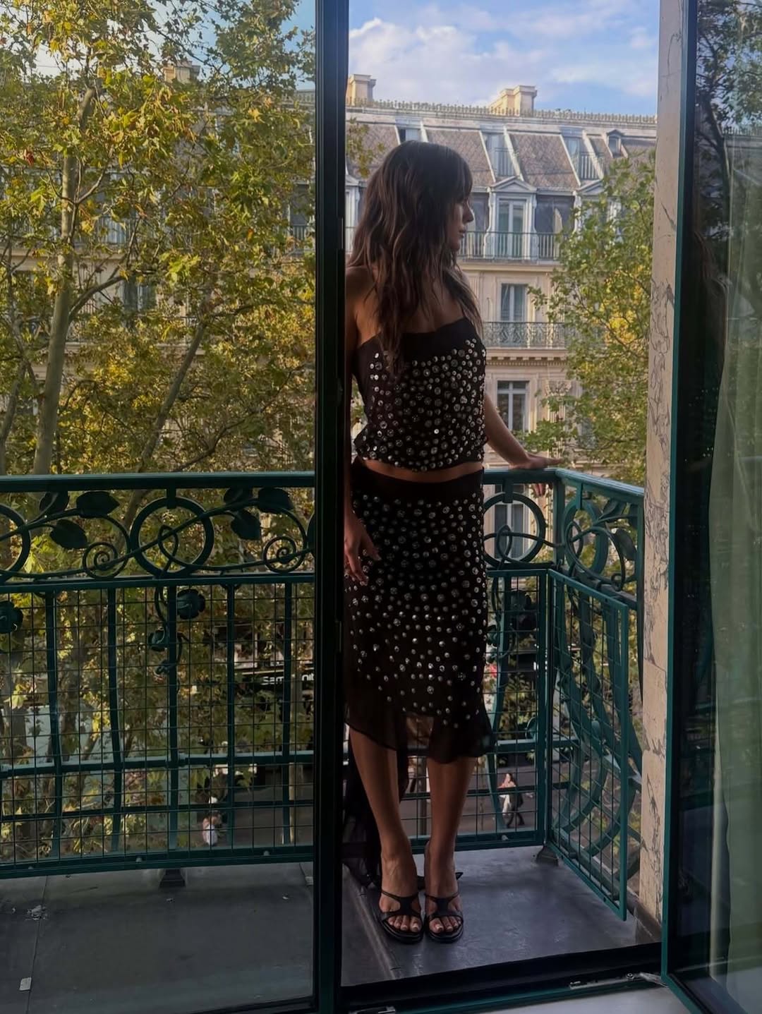 Side profile view on a balcony showing the full length of the embellished skirt and fitted top.