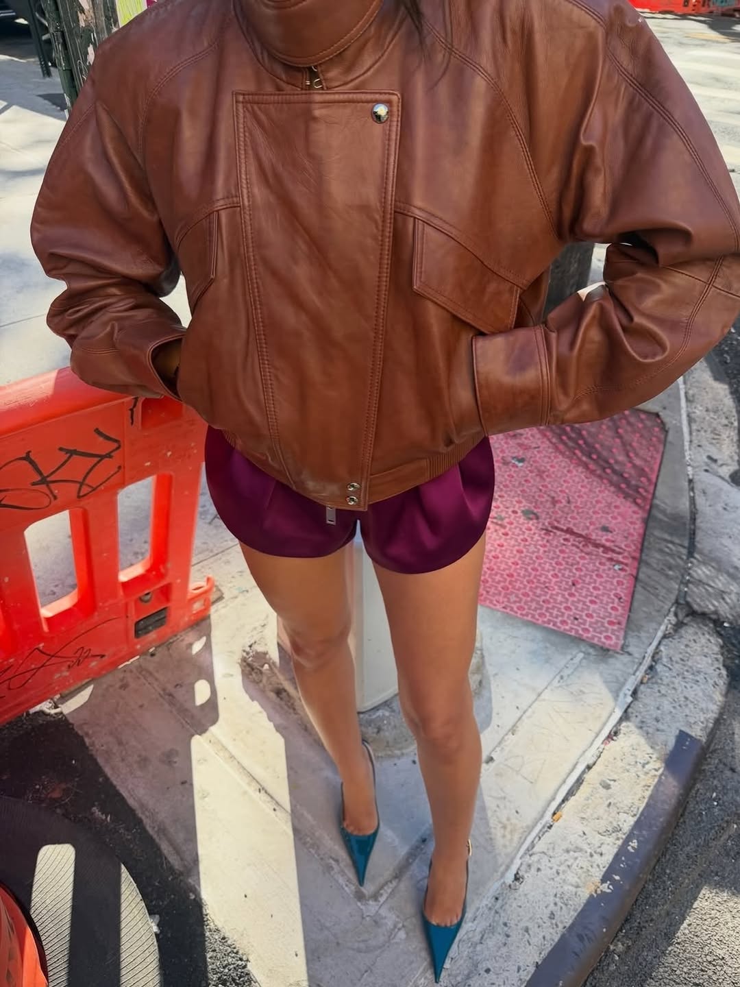 High-angle close-up focusing on the details of the brown leather jacket's hardware and texture paired with the red shorts.