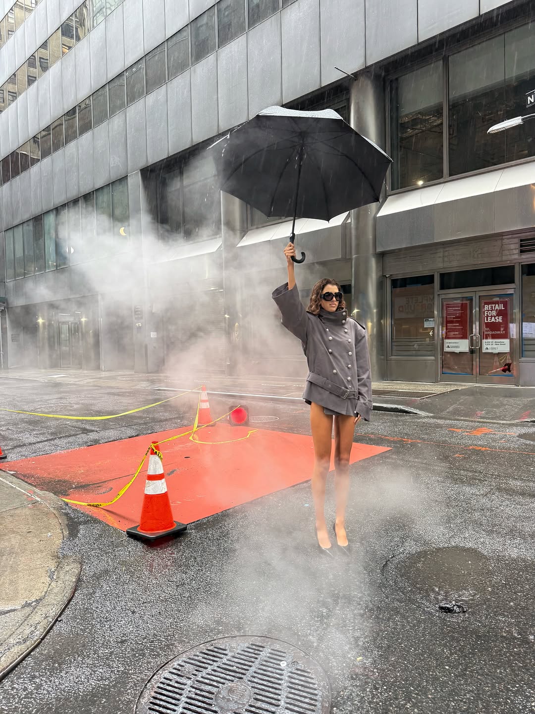 Wide shot of the model raising an umbrella while wearing the grey outfit.
