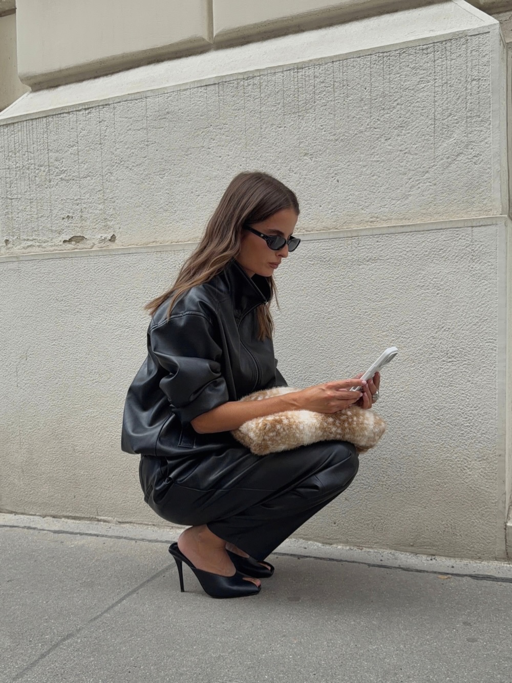 Crouching pose displaying the full silhouette of the leather separates, including the trousers and mule heels.