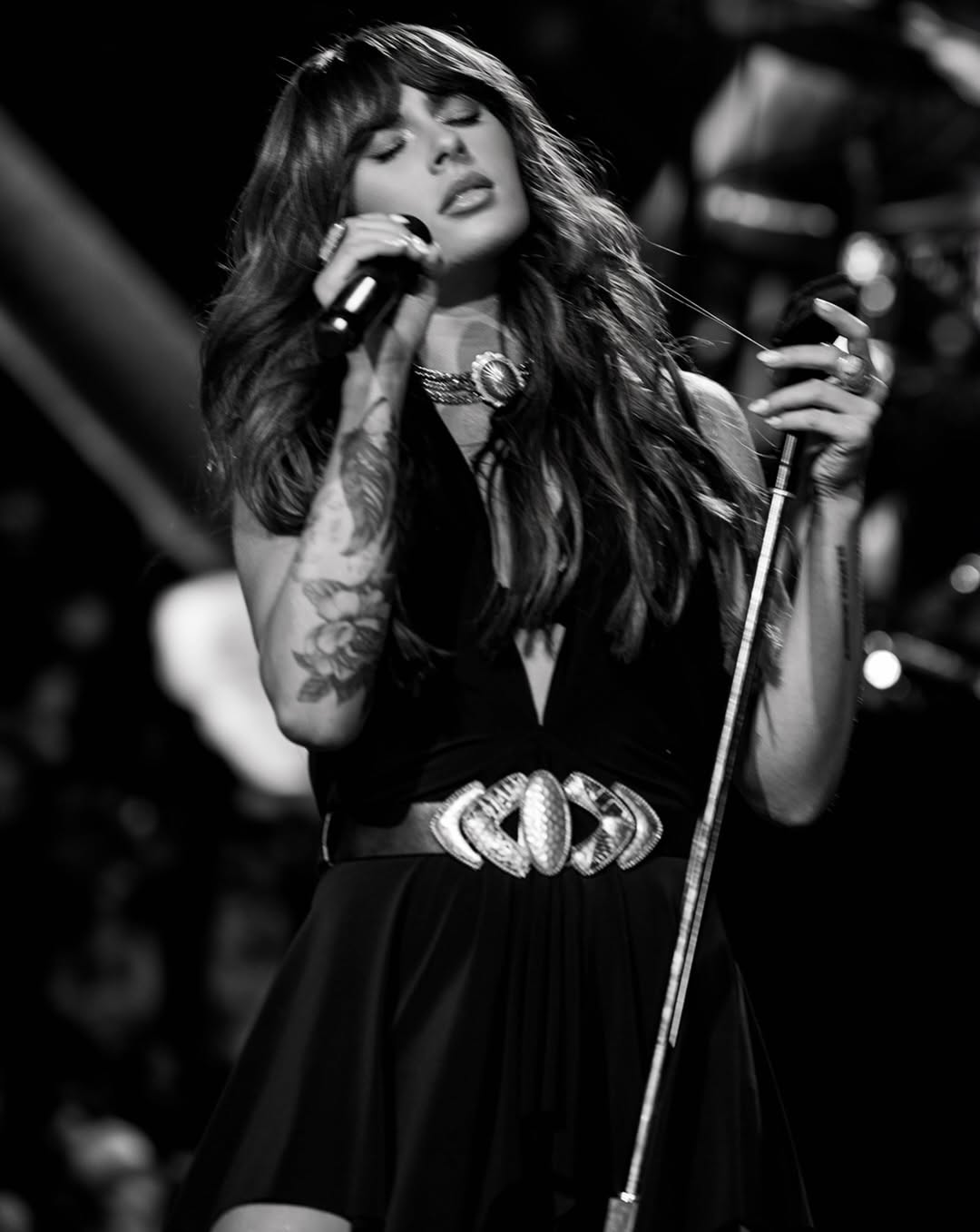 Black and white close-up singing into a mic, focusing on the upper bodice and necklace.