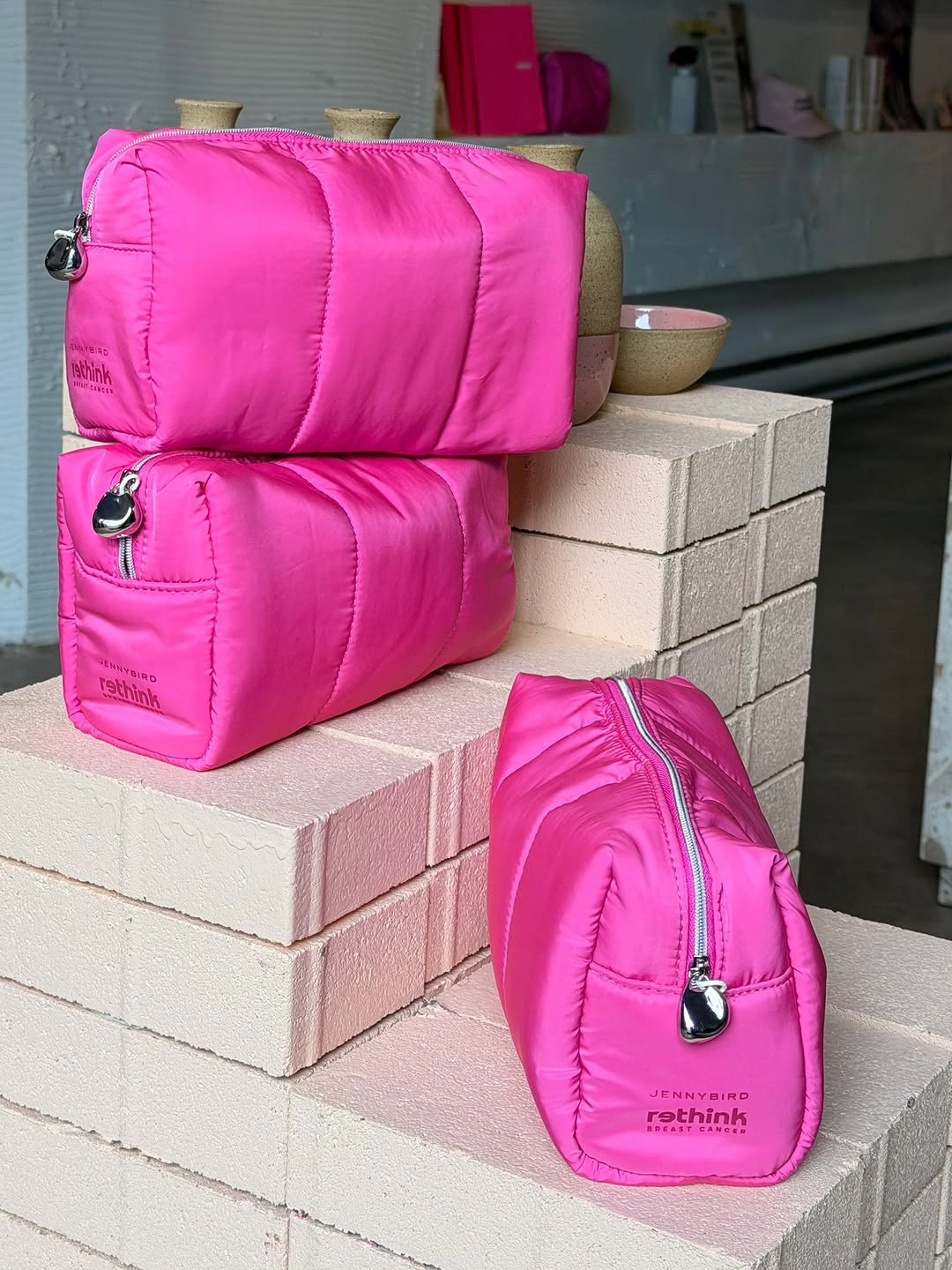 Three identical hot pink puffy pouches stacked on light pink bricks.
