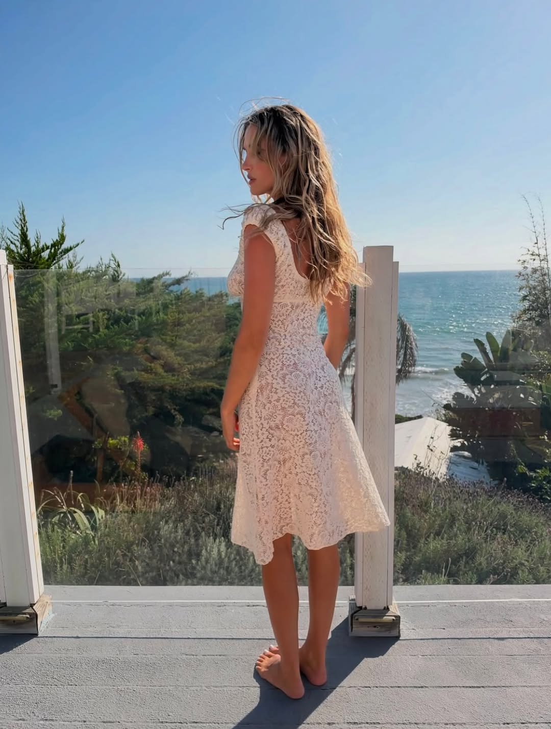 Rear view of model wearing the cream lace dress by the sea.