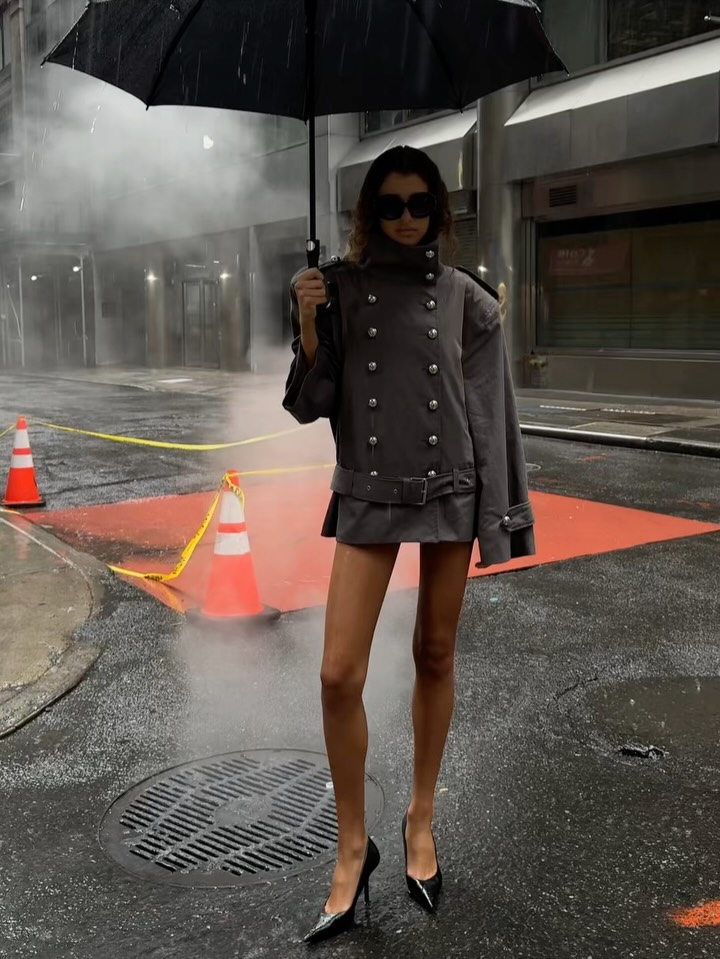 Full body shot of the model standing on a wet street in the same grey outfit.