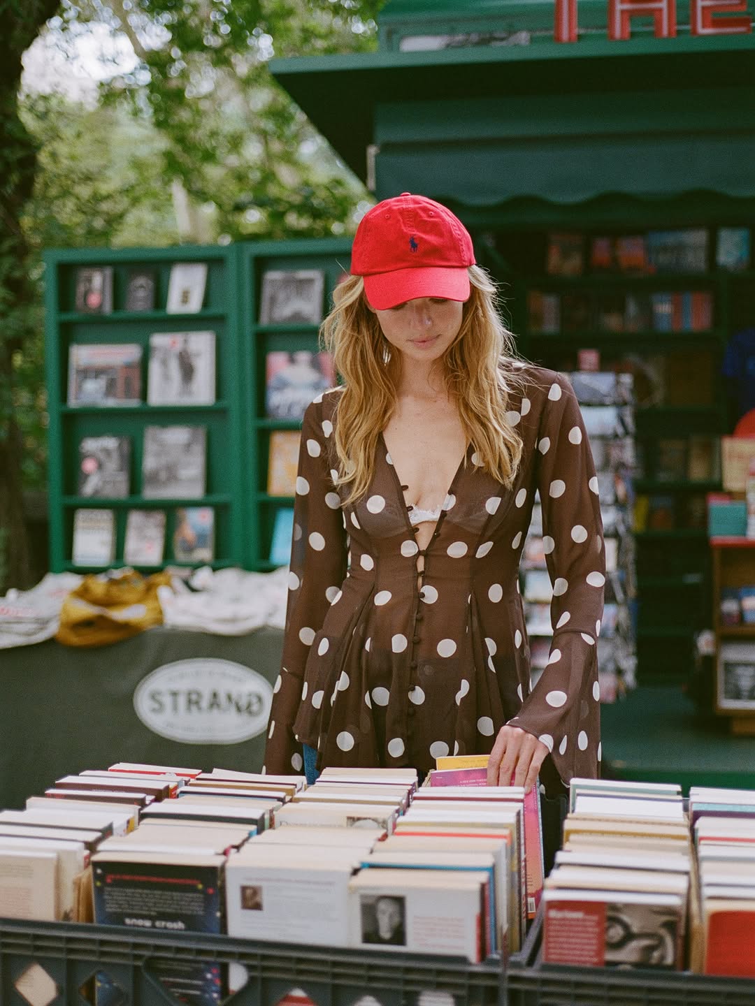 Medium shot of the same woman in the brown polka-dot blouse and red cap, looking down at books.